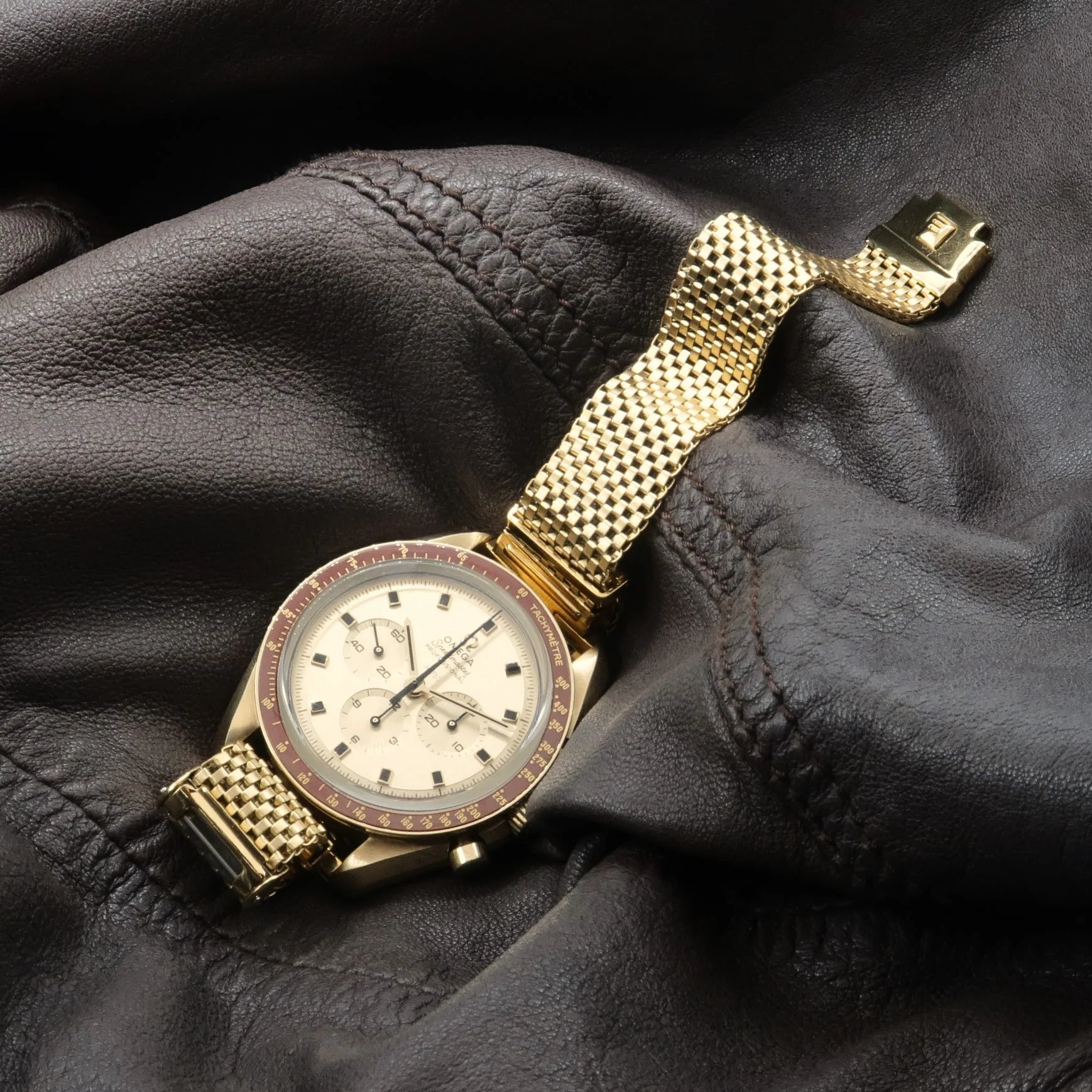 Gold plated mesh watch with red bezel and cream dial on black leather background