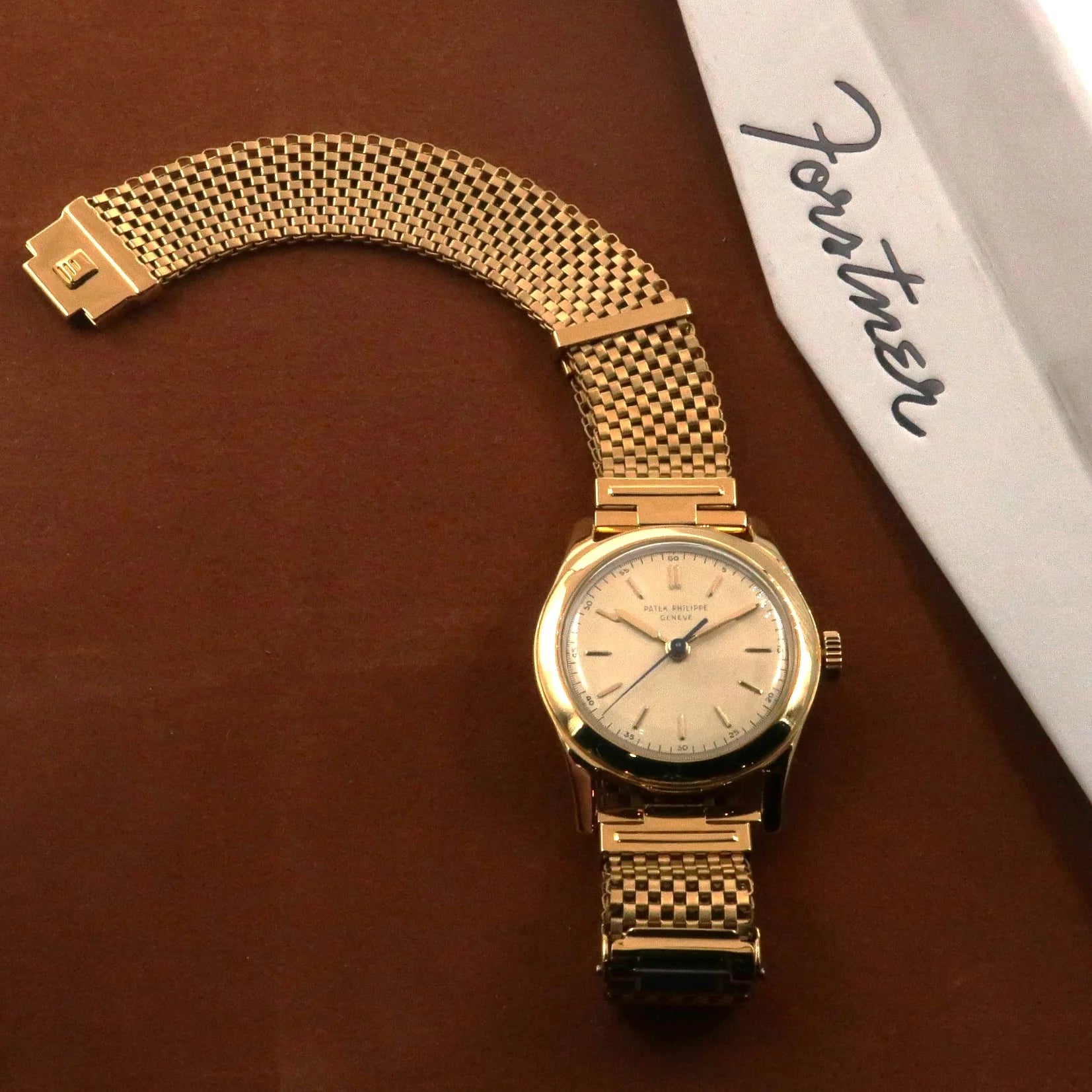 Gold plated mesh watch bracelet with straight ends and integrated clasp on brown leather background