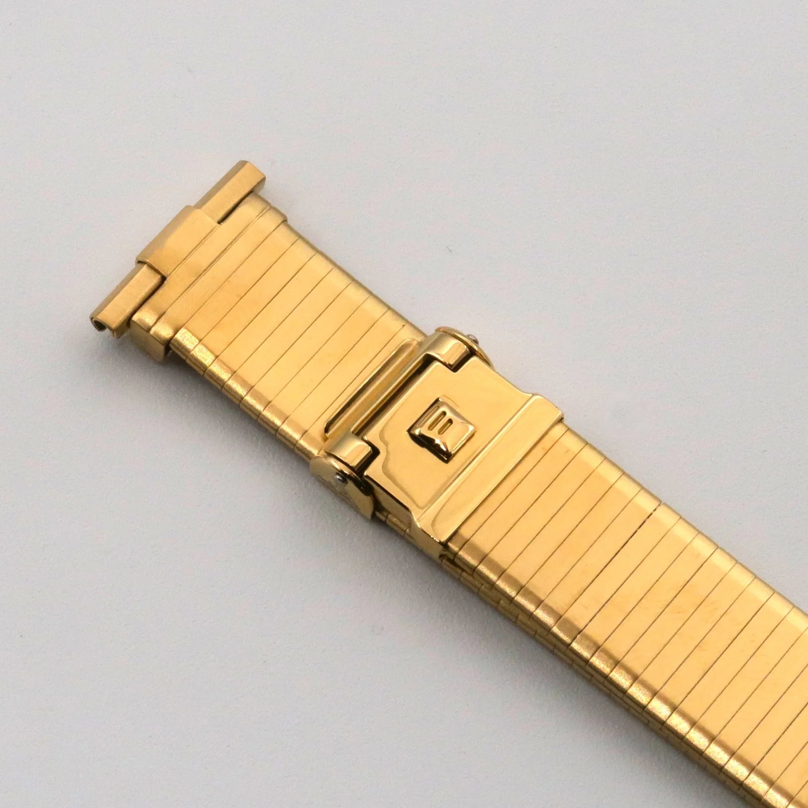 Gold plated expandable metal watch band with fold-over clasp and ridged links on white background