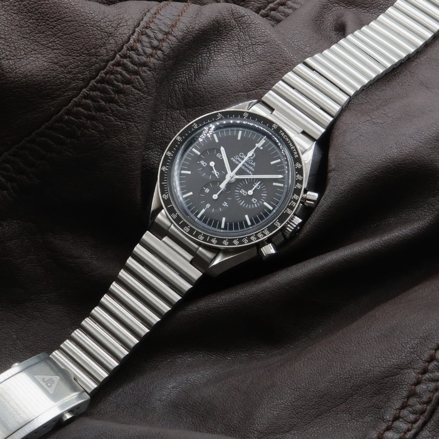 Omega Speedmaster chronograph watch with black dial and steel barrel bracelet on brown leather background