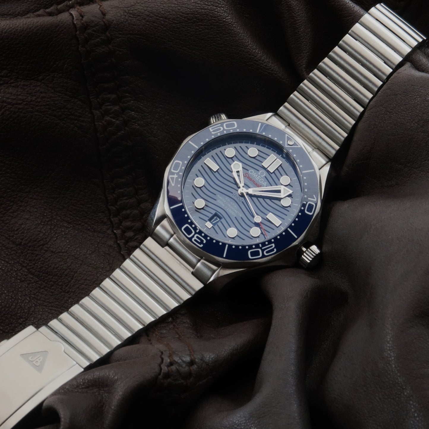 Forstner stainless steel barrel bracelet on Omega Seamaster dive watch with blue dial, displayed on black leather jacket