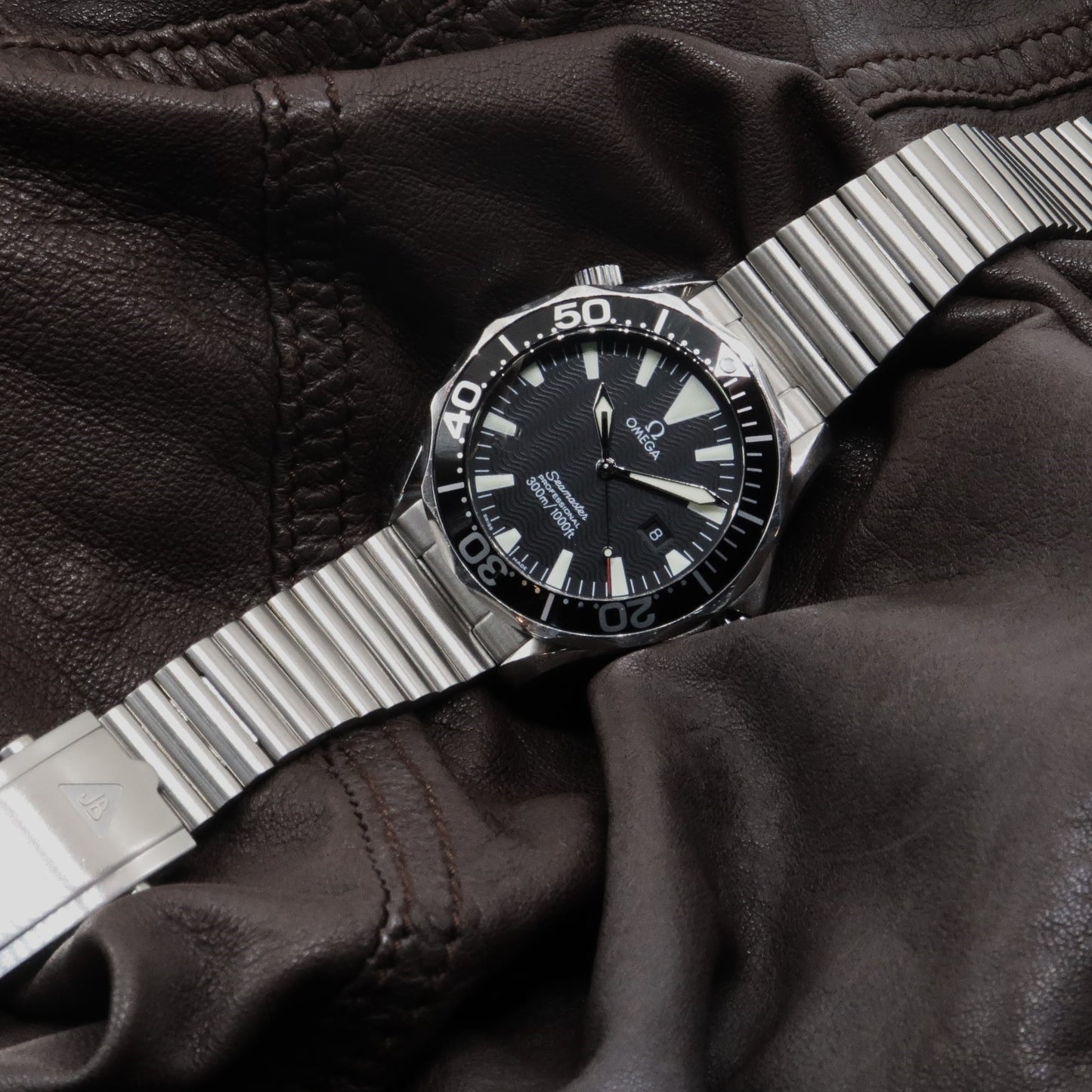Stainless steel barrel bracelet on Omega Seamaster dive watch with black dial and leather gloves