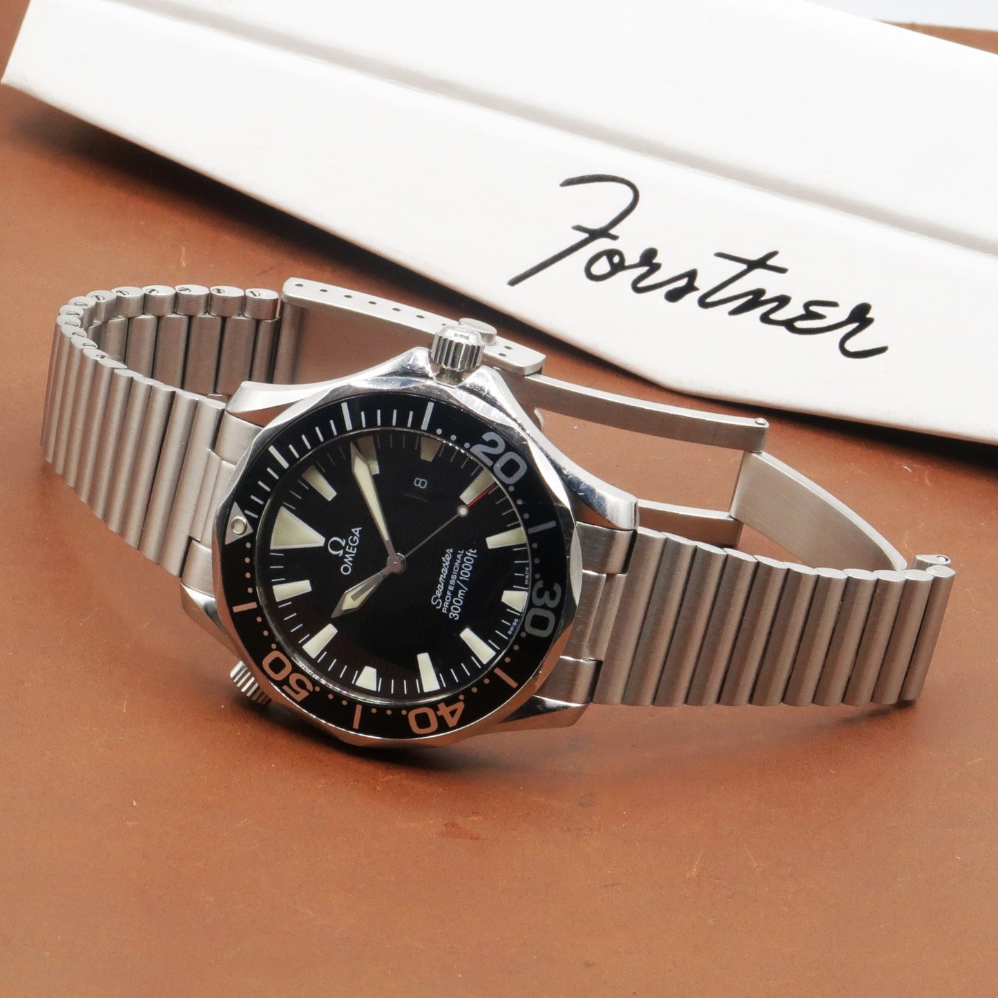 Omega Seamaster watch with black dial and orange bezel on silver stainless steel barrel bracelet