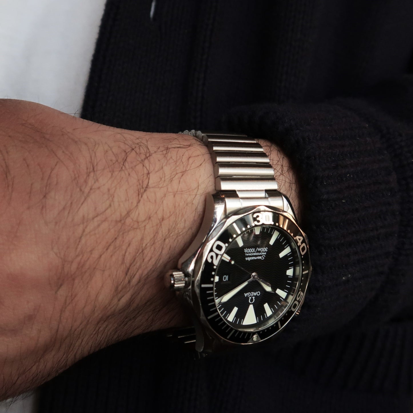 Men's Omega Seamaster dive watch with stainless steel barrel bracelet worn on wrist with black sweater