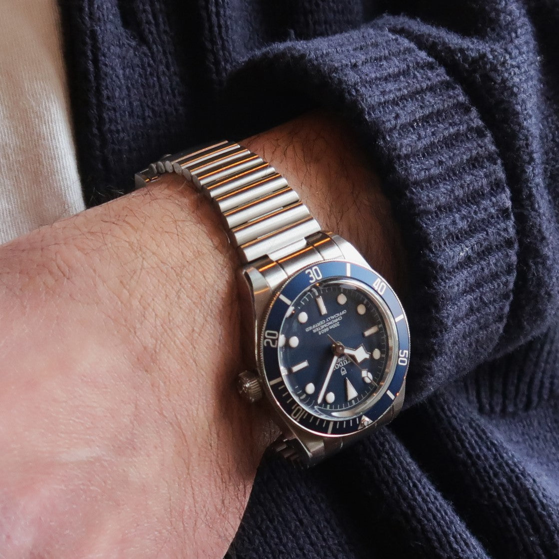 Two-tone stainless steel barrel bracelet with end links on Tudor Black Bay watch, worn on wrist with navy sweater