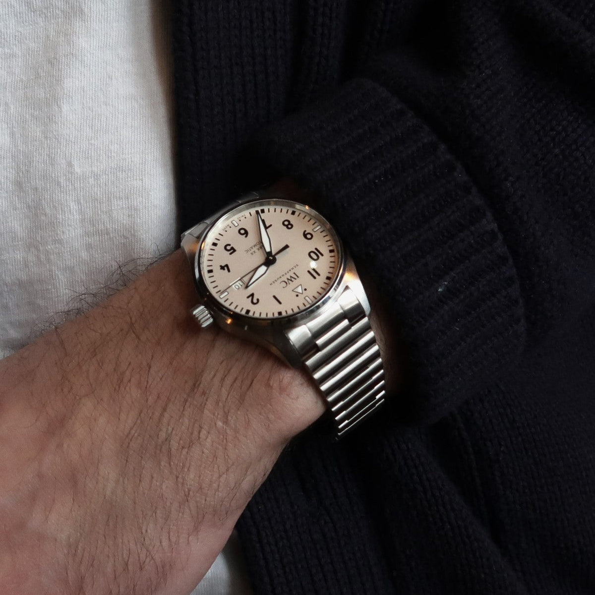 Silver stainless steel watch with cream dial and barrel bracelet worn on wrist with white and black sleeves