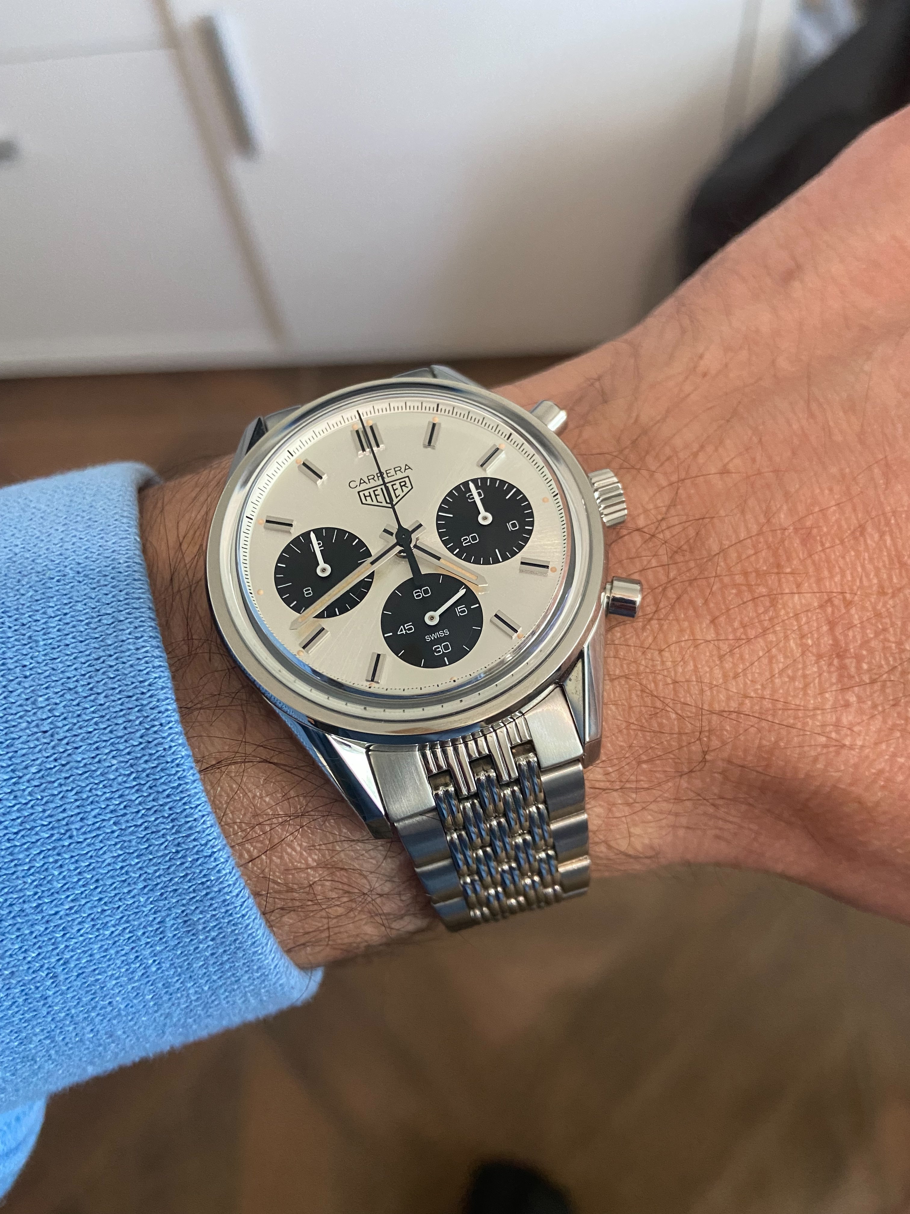 Carrera chronograph watch with cream dial, black subdials, steel bracelet worn on wrist with blue shirt
