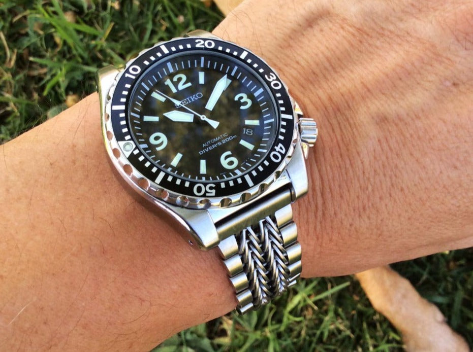 Seiko automatic dive watch with black dial and rotating bezel on two-tone stainless steel razor-wire bracelet, worn on wrist