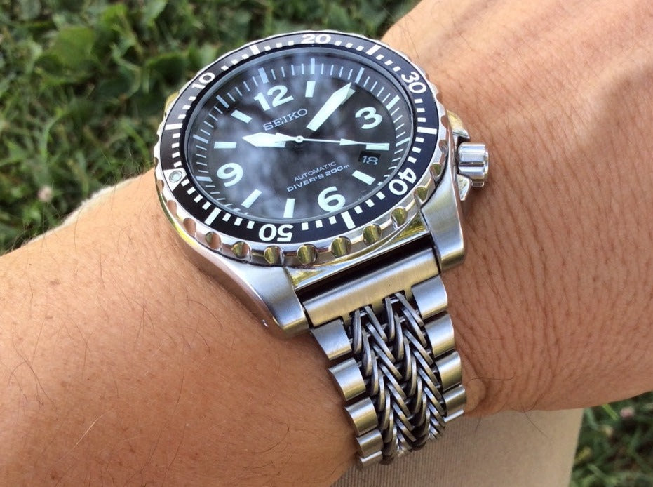 Seiko automatic diver watch with stainless steel razor-wire straight end bracelet on wrist against green outdoor background