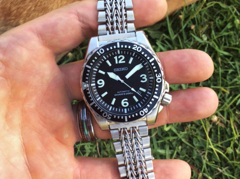 Seiko automatic diver's watch with black dial and stainless steel mesh bracelet held in hand outdoors