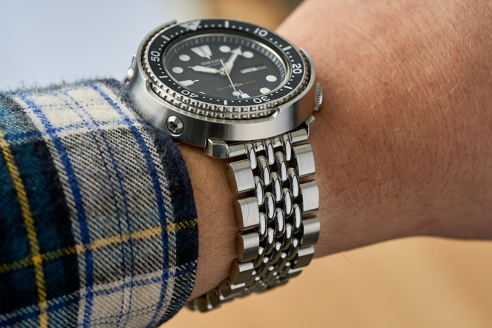 Stainless steel dive watch with black dial and rotating bezel on men's wrist with plaid sleeve