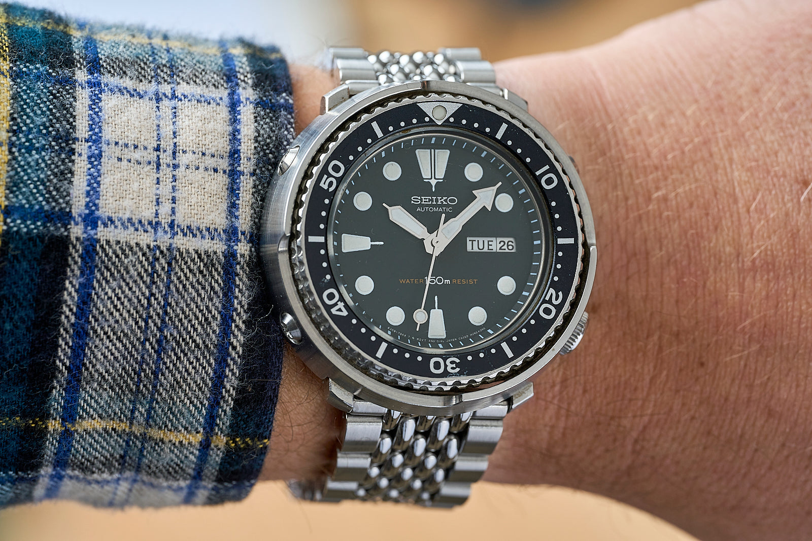 Seiko automatic dive watch with black dial, steel bracelet and bezel on wrist wearing blue plaid shirt