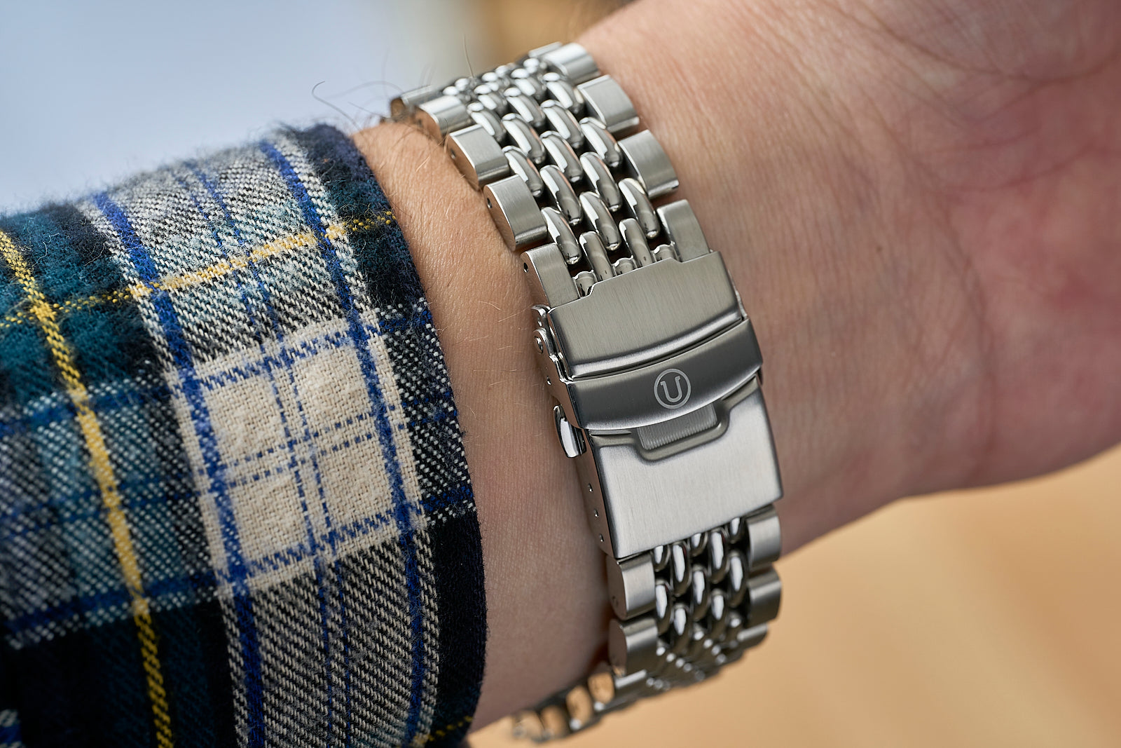 Stainless steel beads of rice bracelet with straight end links worn on wrist with plaid sleeve, showing metal clasp and articulated chain design