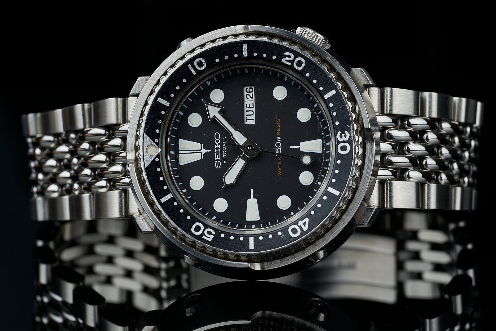 Seiko automatic dive watch with black dial, luminous indices, rotating bezel, and stainless steel bracelet on black background