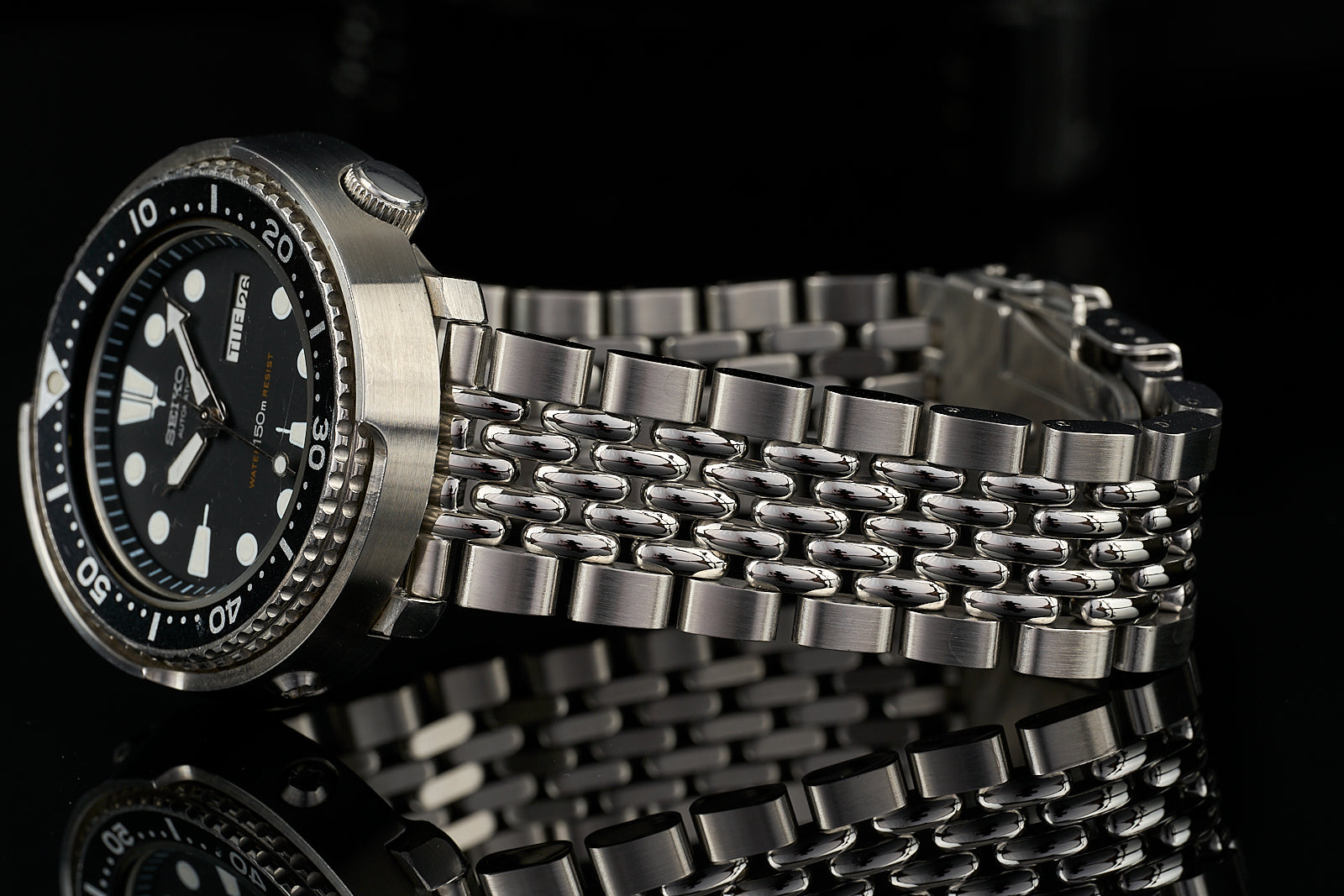 Stainless steel diver watch with black dial and beads of rice bracelet on black background