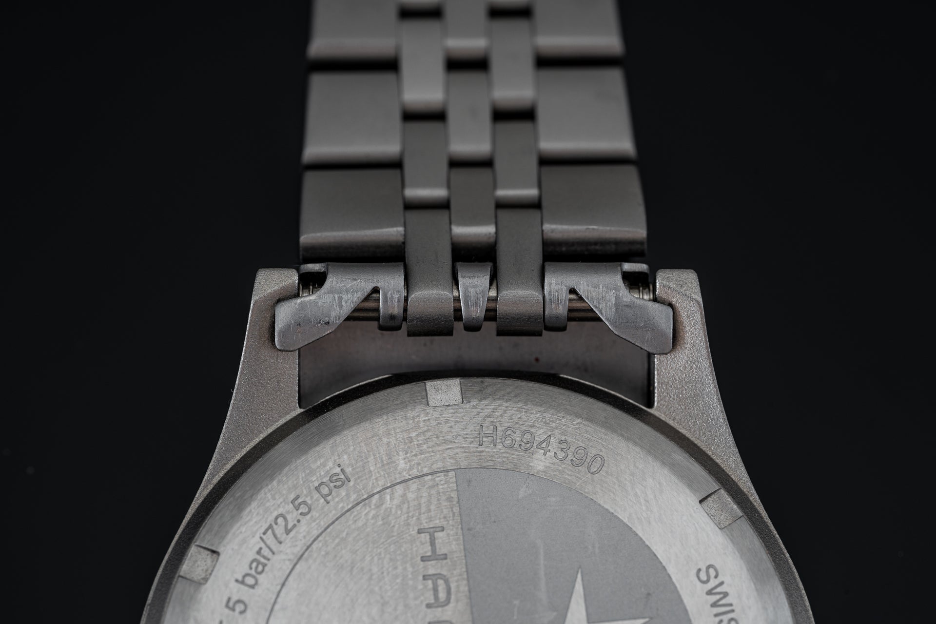 Stainless steel bracelet with linked segments attached to Hamilton Khaki mechanical watch case, showing caseback engravings and specifications