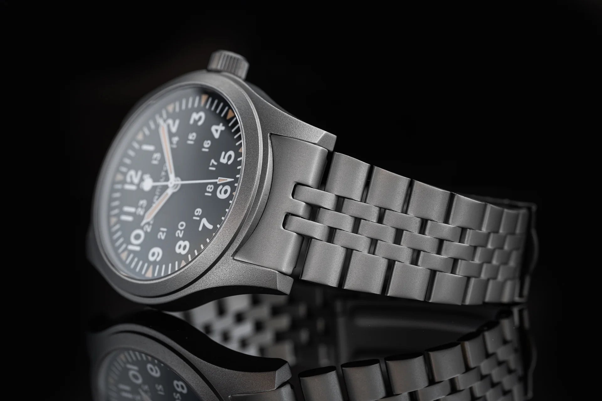 Stainless steel mechanical watch with black dial, Arabic numerals, and matching metal bracelet on reflective surface