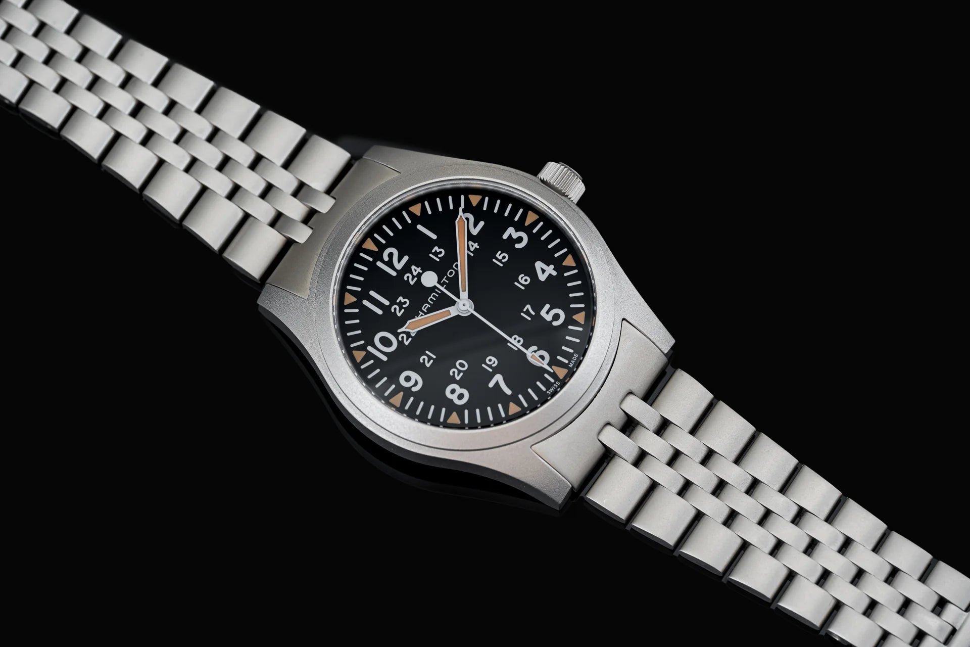 Stainless steel field watch with black dial, Arabic numerals, and matching metal bracelet on black background