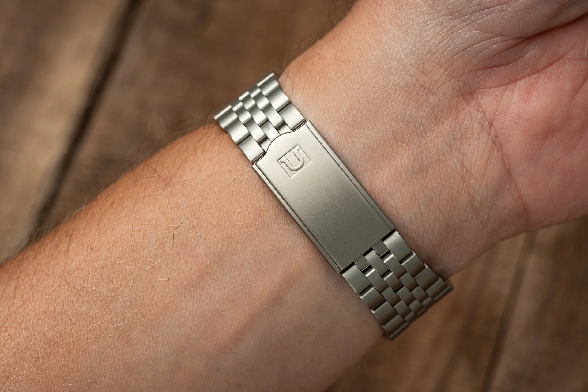 Silver stainless steel bracelet with engraved logo worn on wrist, matching metal band watch accessory