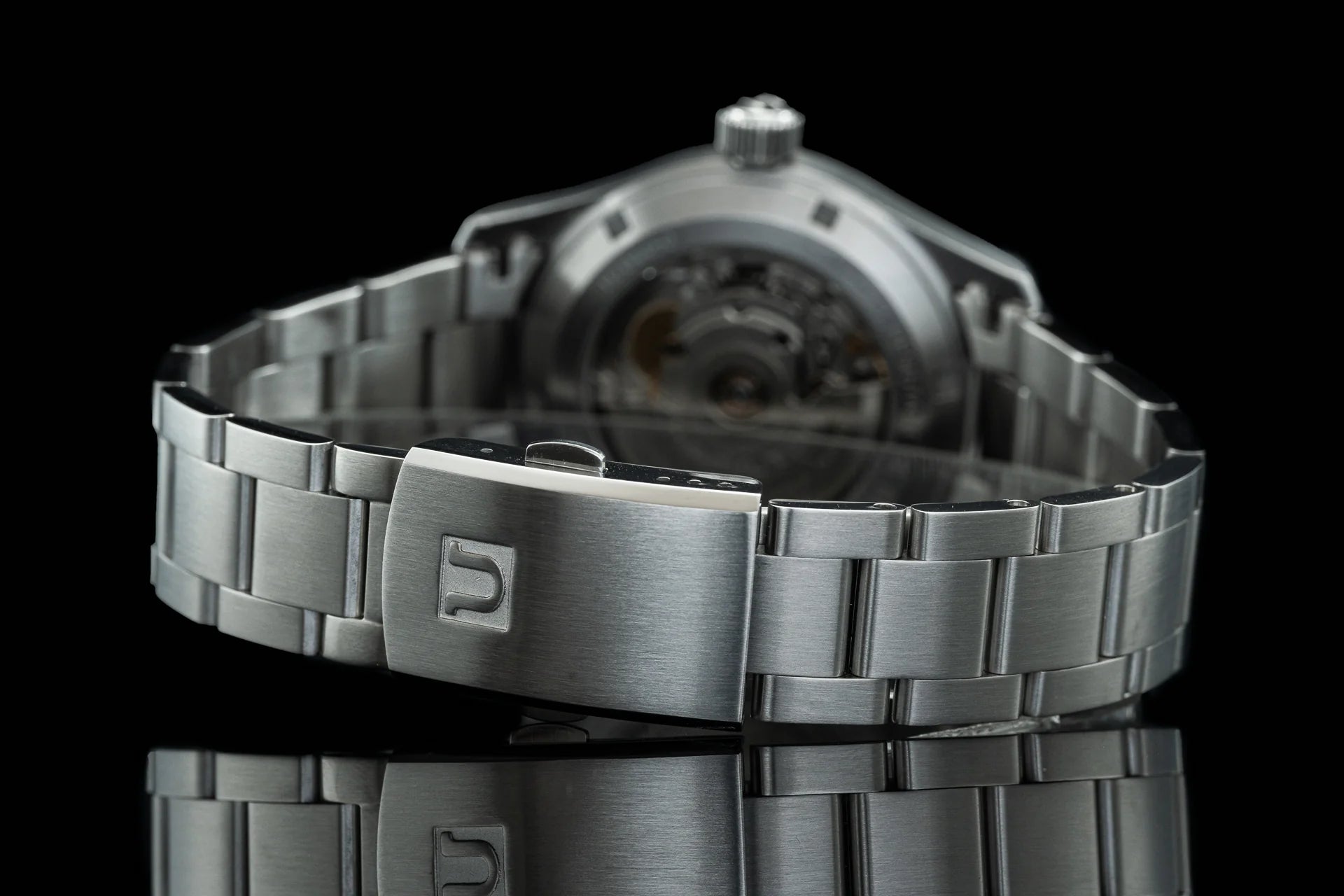 Stainless steel automatic watch with metal bracelet and deployant clasp, showcasing polished case and brushed links against black background