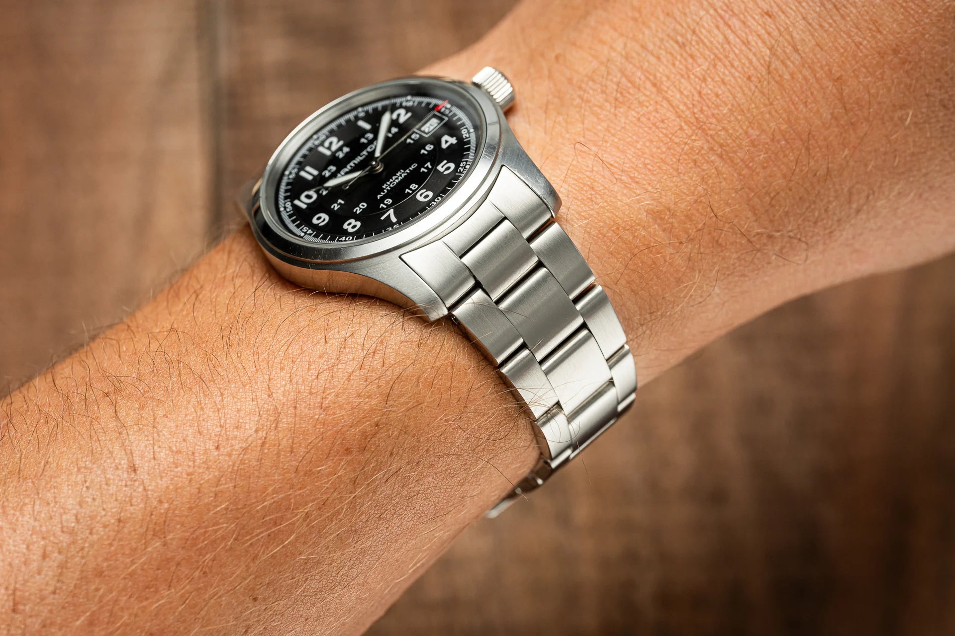 Stainless steel automatic watch with black dial worn on wrist, featuring bracelet band and date window