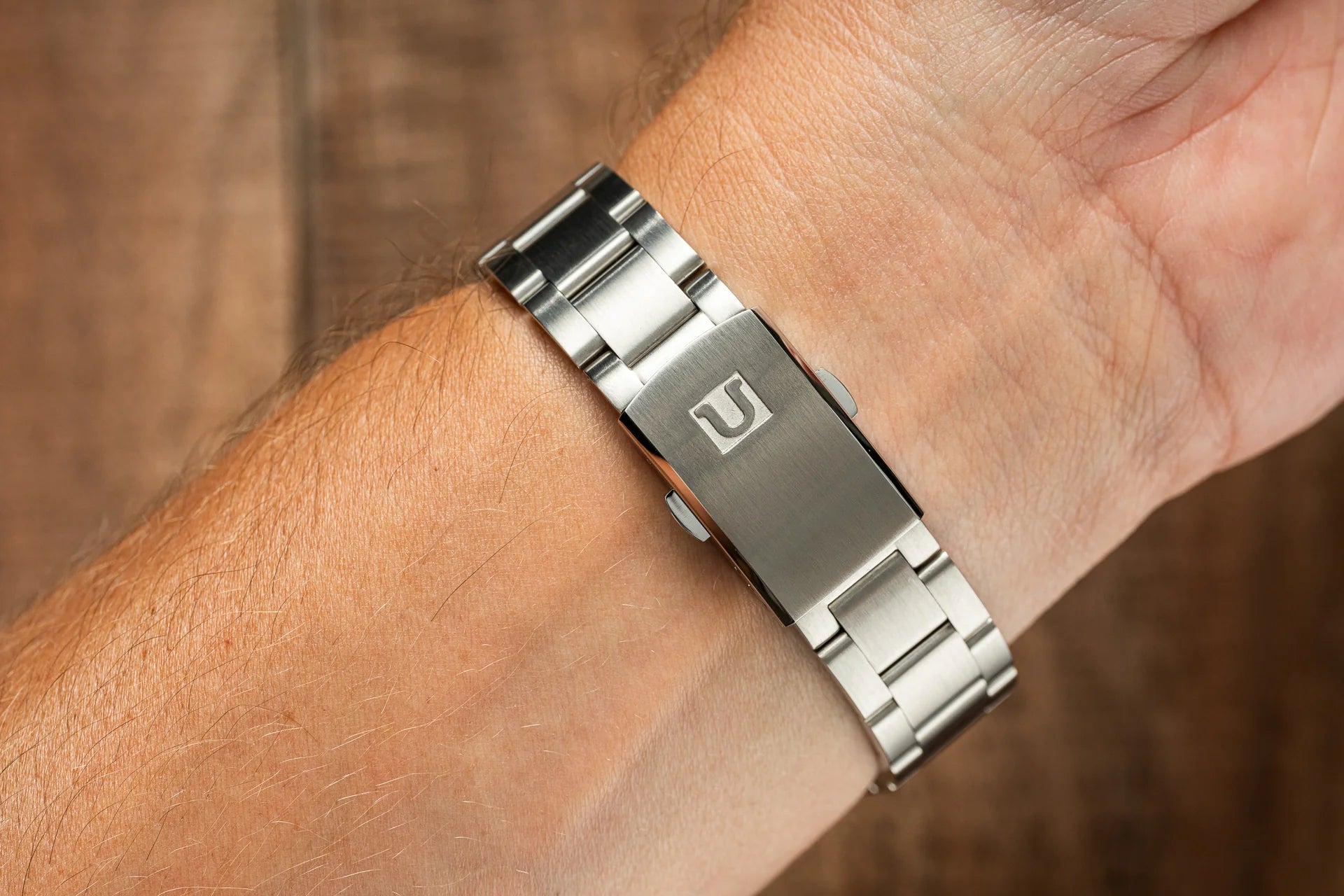 Two-tone stainless steel bracelet with brushed center link and polished edges worn on wrist, featuring logo clasp