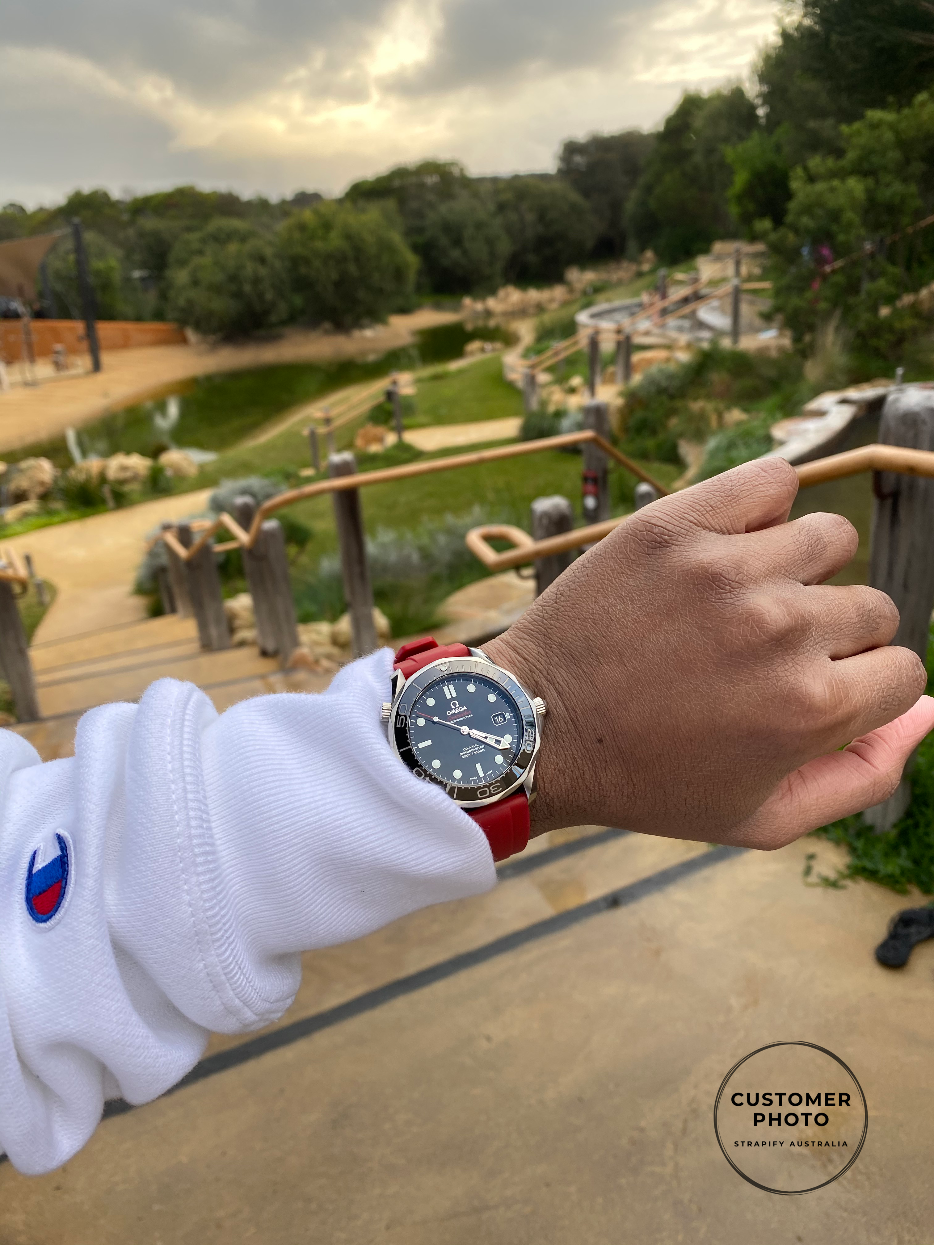 Luxury dive watch with black dial and red quick release FKM rubber strap worn on wrist at scenic outdoor location