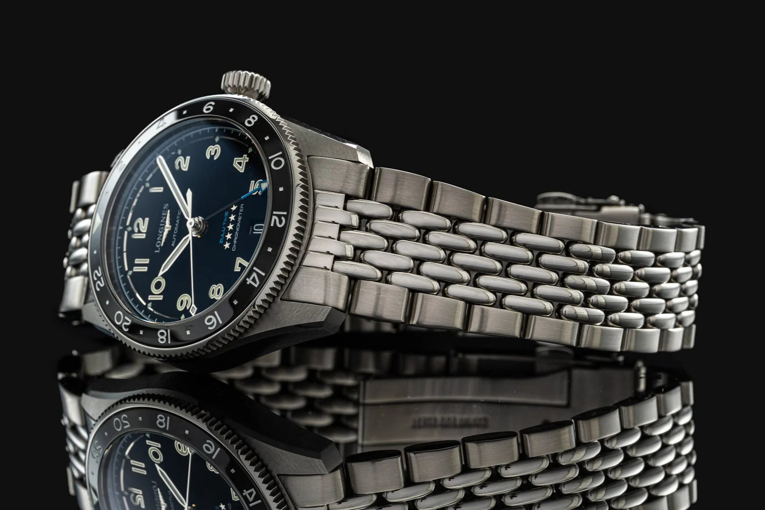 Longines Spirit Zulu Time 39mm stainless steel watch with dark blue dial and beads of rice bracelet on black background