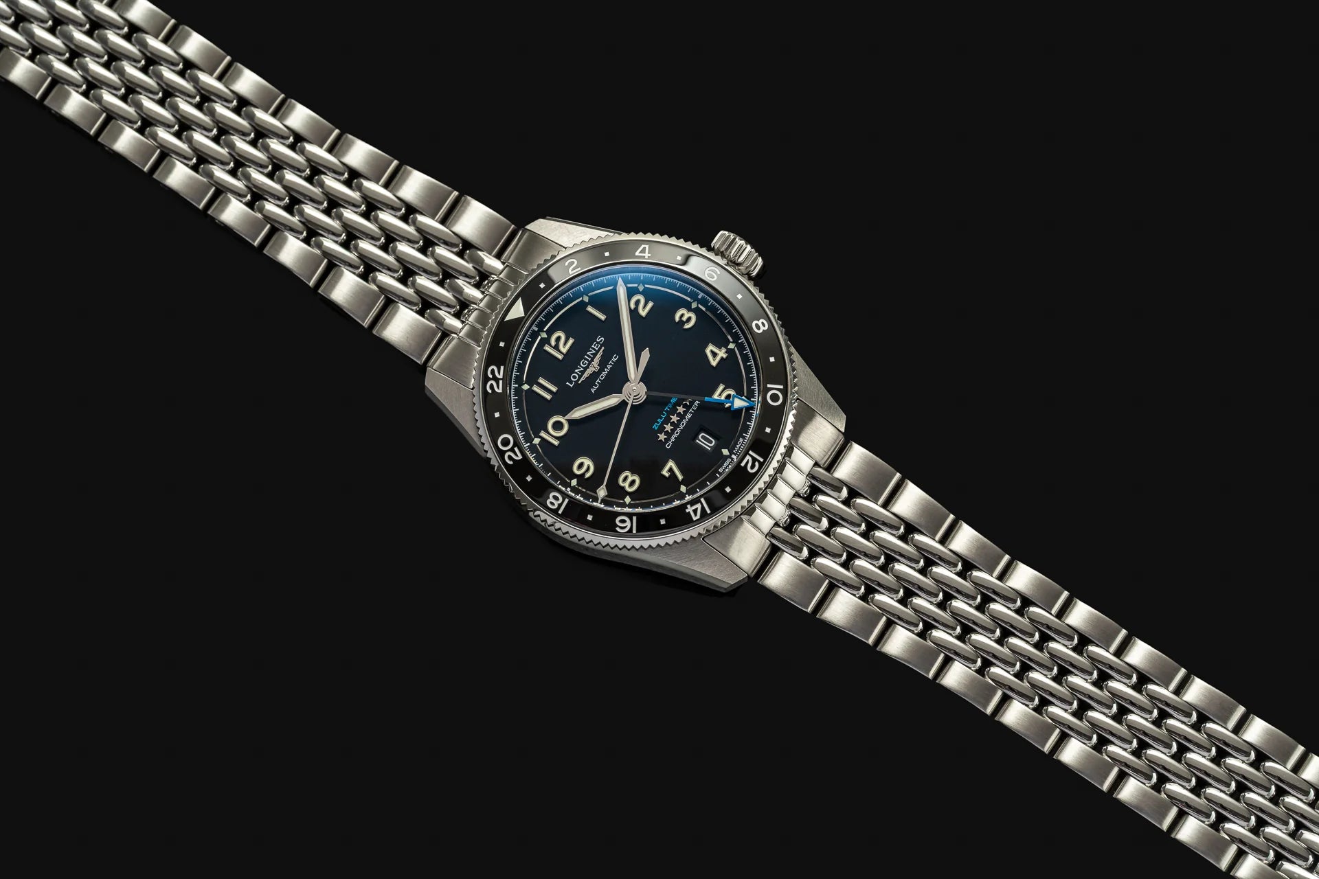 Longines Spirit Zulu Time 39mm watch with stainless steel beads of rice bracelet, dark blue dial, and black bezel on black background
