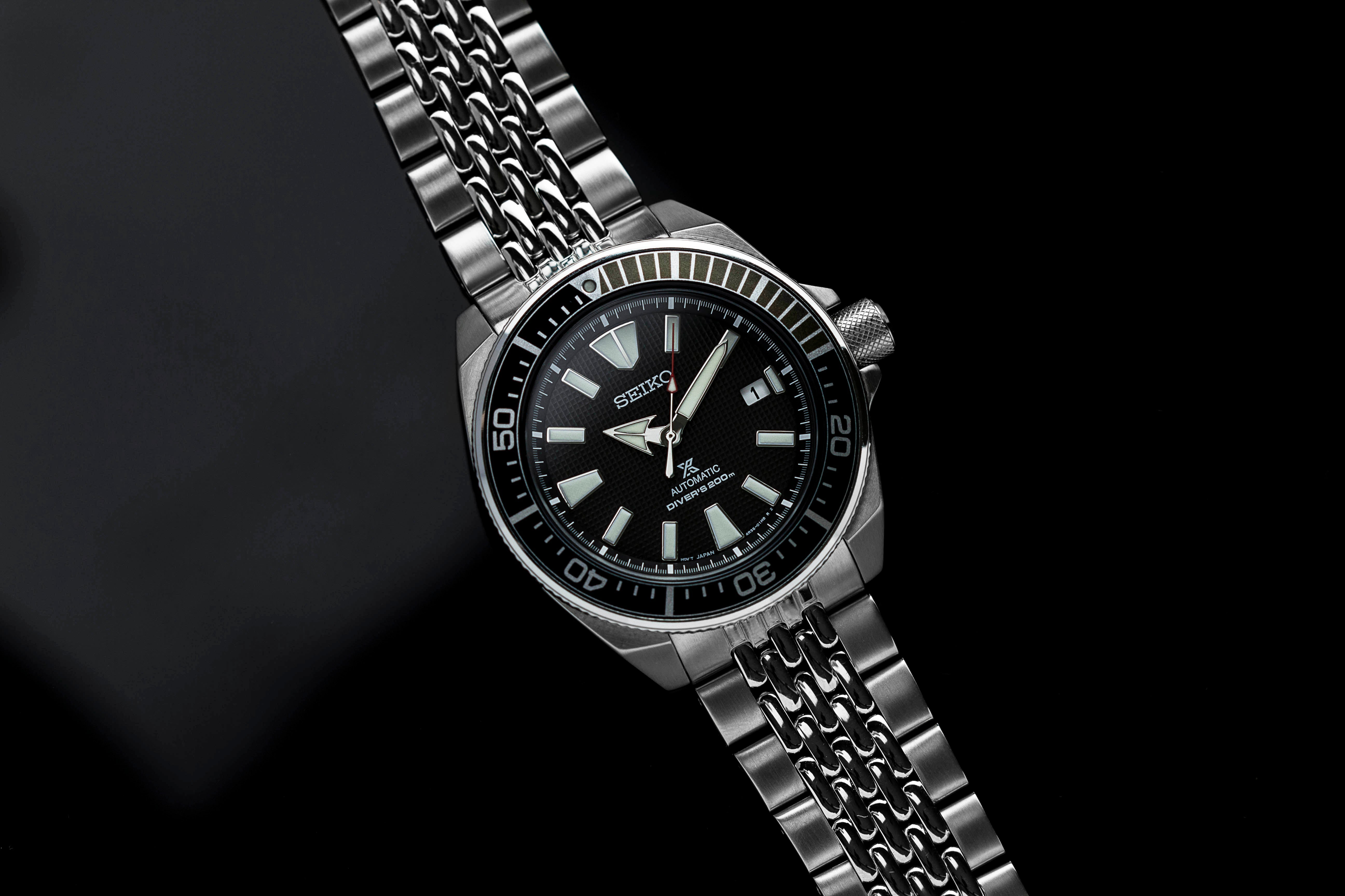 Seiko Samurai automatic dive watch with black dial, stainless steel beads of rice bracelet, and rotating bezel on dark background