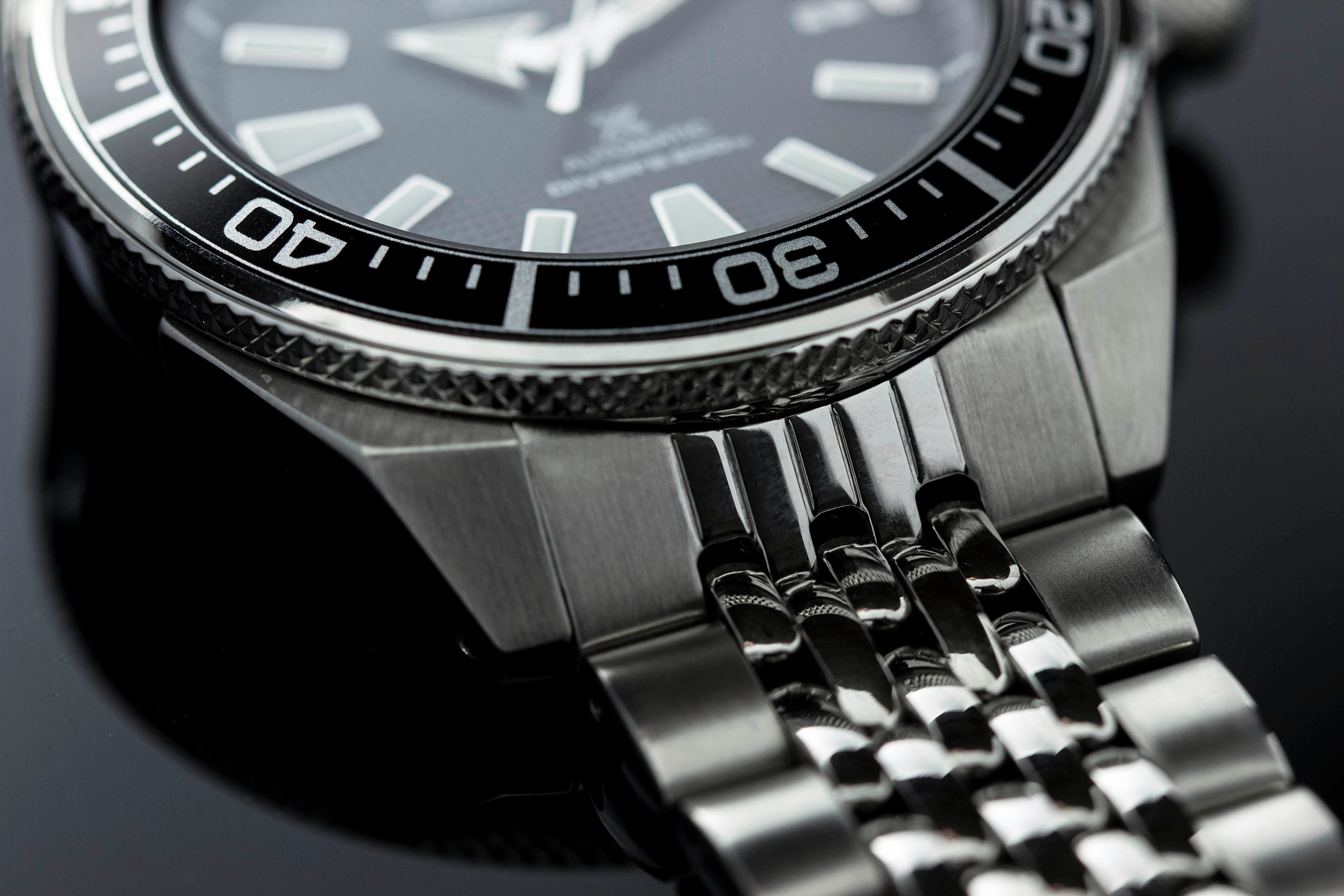 Stainless steel dive watch with black dial, white markers, rotating bezel, and brushed metal bracelet with solid link design