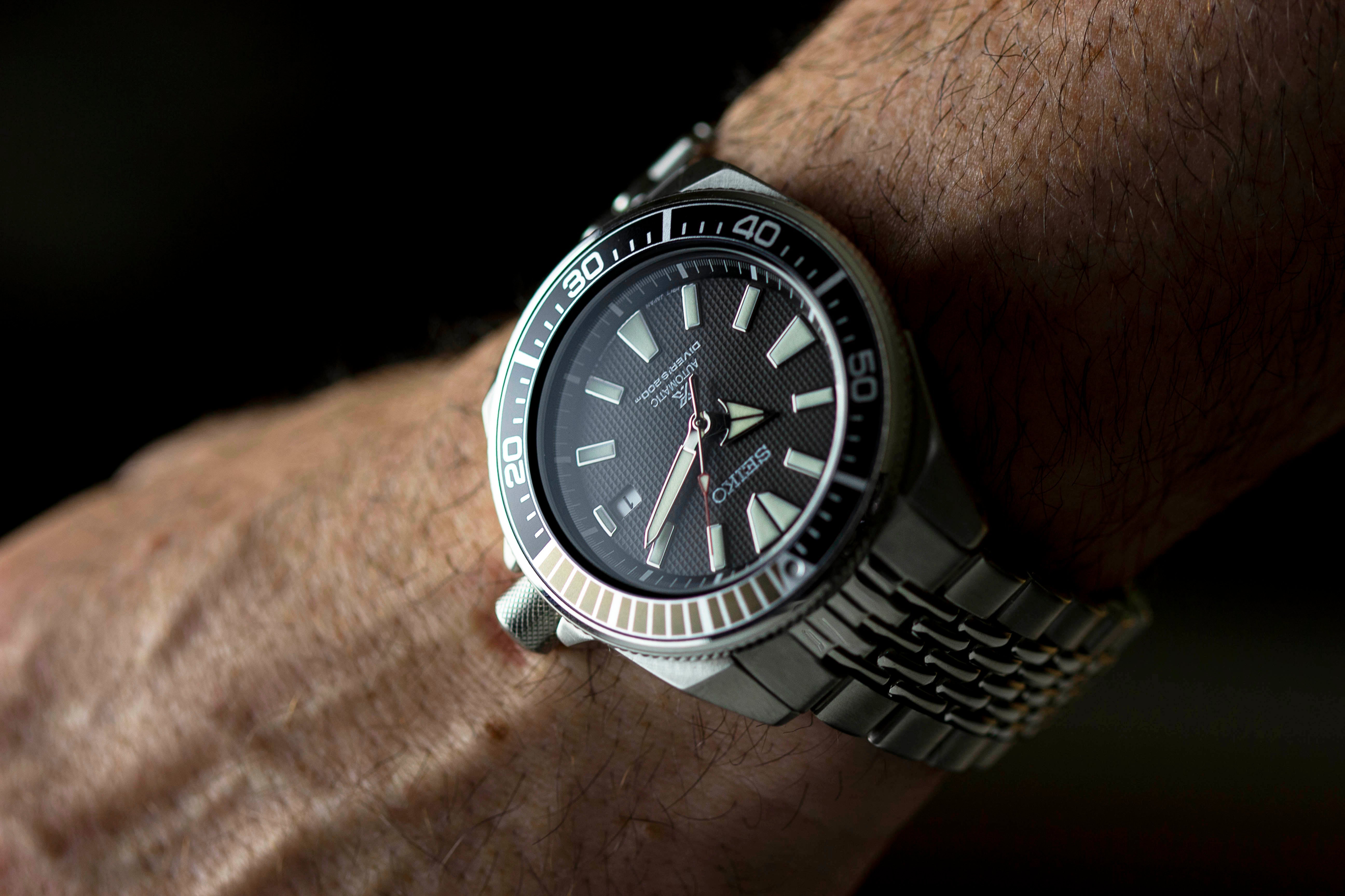 Men's stainless steel sports watch with black dial, luminous hour markers, tachymeter bezel, and metal bracelet worn on wrist
