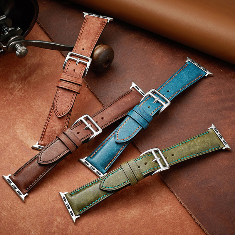 Leather Apple Watch bands in brown, blue, and olive green with silver connectors displayed on tan leather background