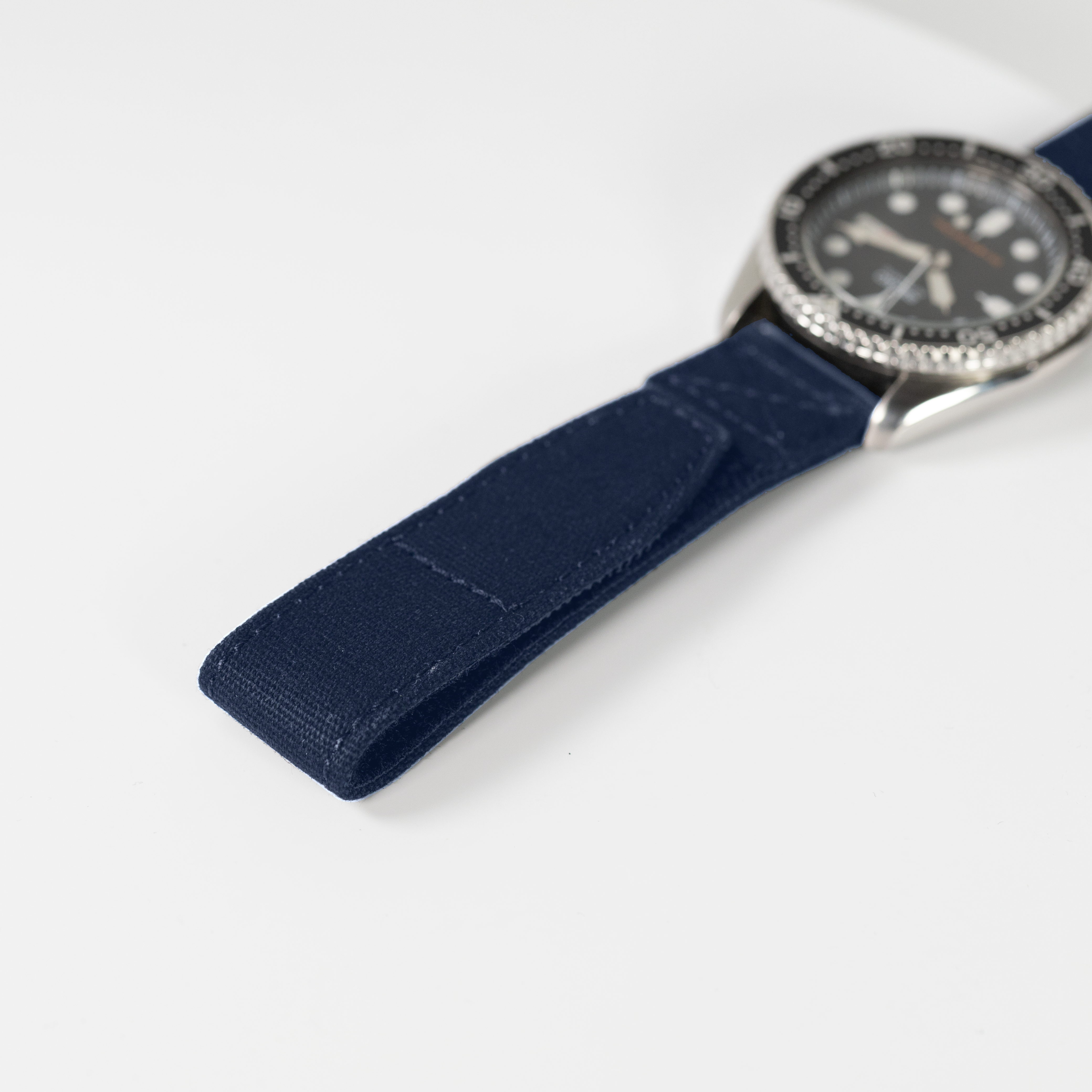 Military style watch with navy blue quick release velcro strap and black dial with silver bezel on white background