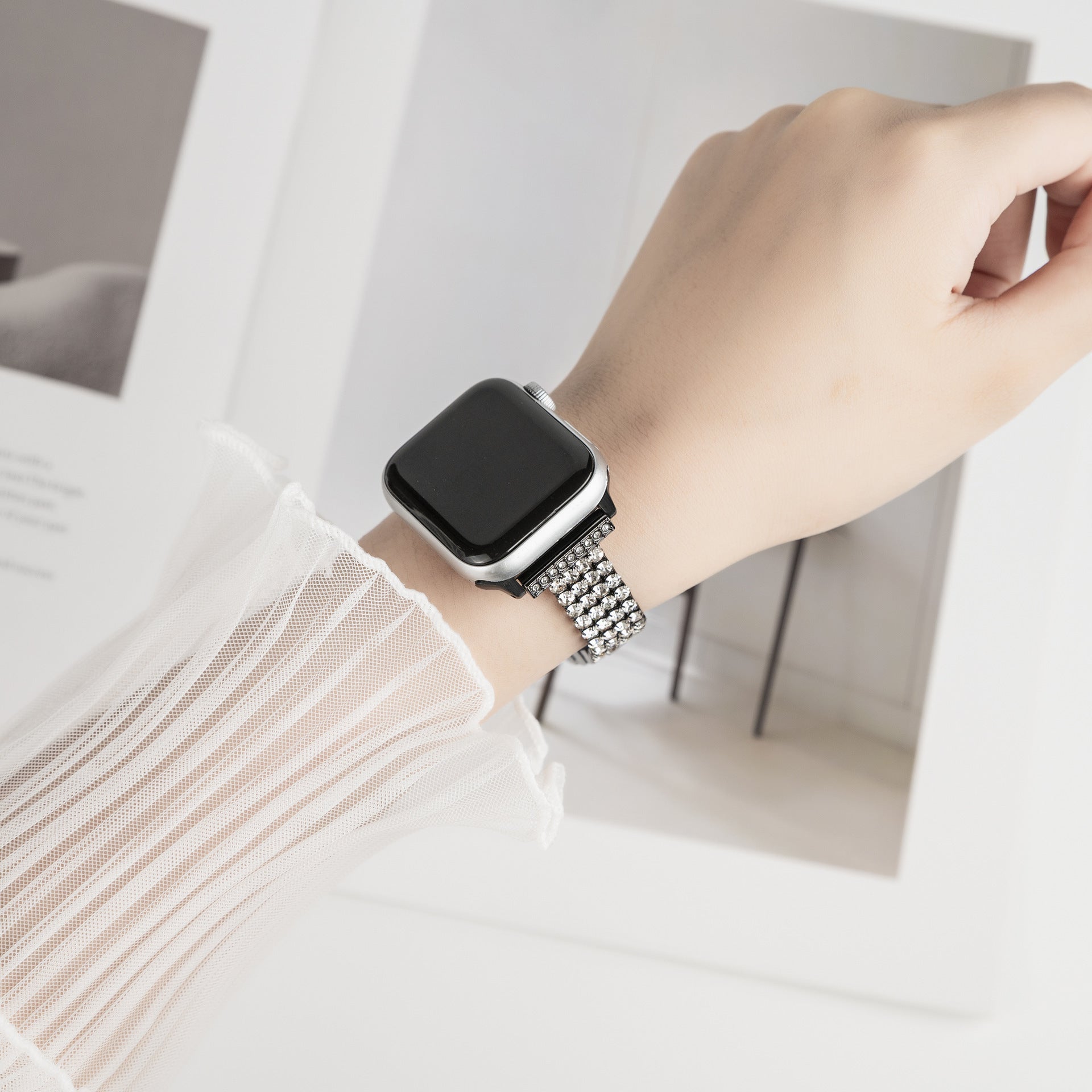 Apple Watch with silver diamond-studded metal bracelet band on woman's wrist, square black face display visible