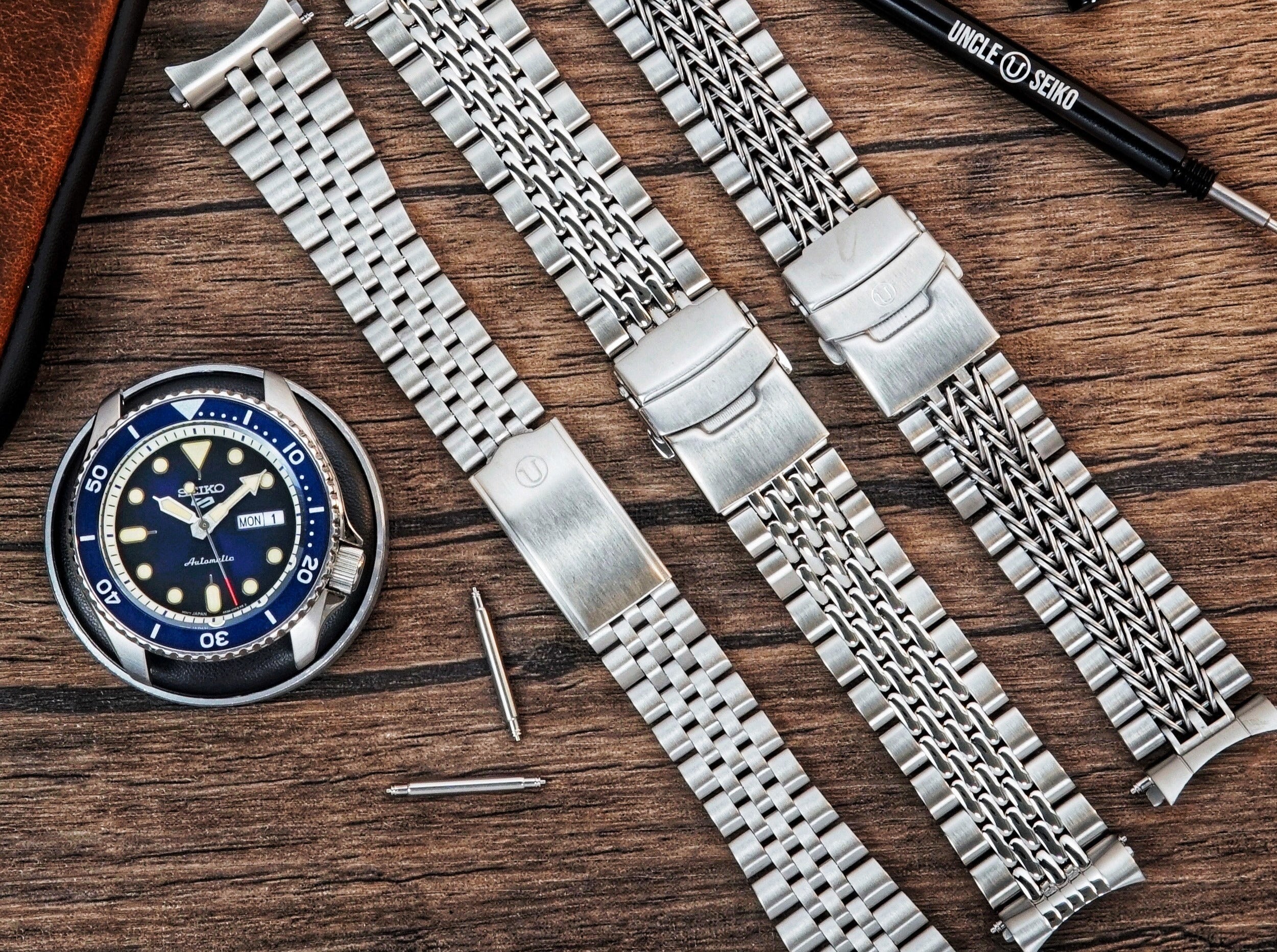Seiko dive watch with blue dial and three stainless steel metal bracelet options displayed on wooden surface with tools