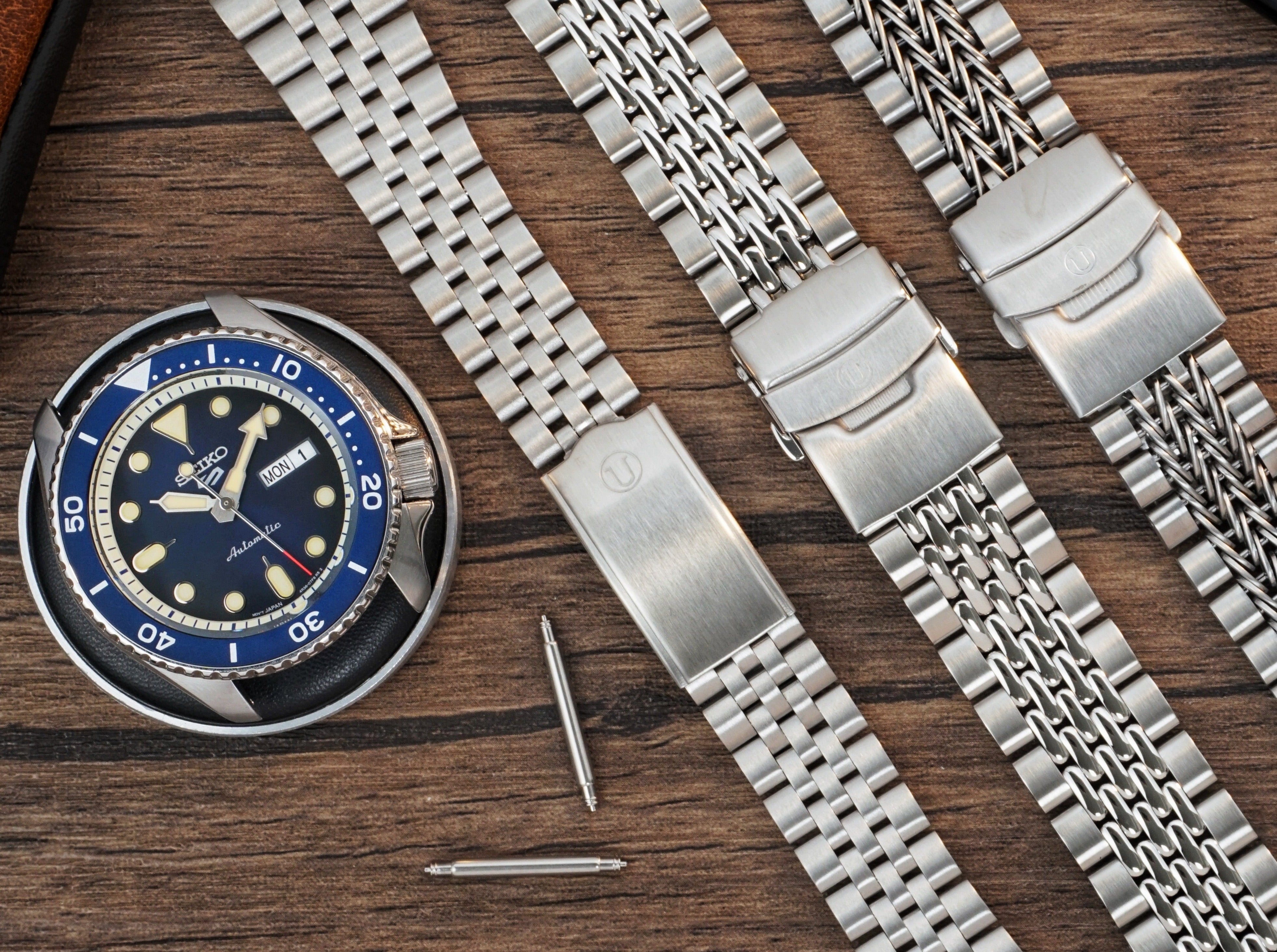 Seiko dive watch with blue bezel and stainless steel bracelets displayed on wooden surface with watch tools
