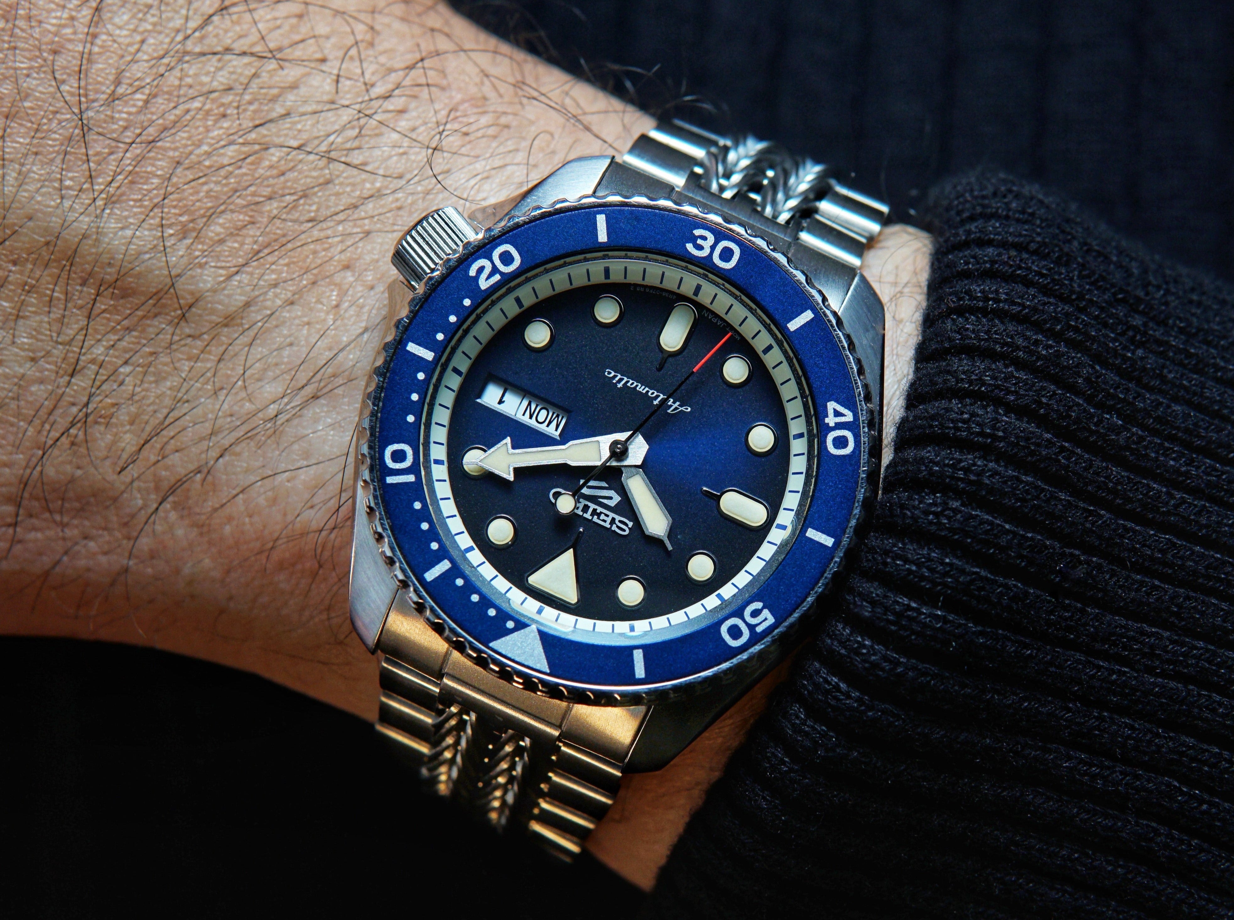 Seiko SRPD automatic watch with blue ceramic bezel, black dial, date window, and stainless steel bracelet worn on wrist