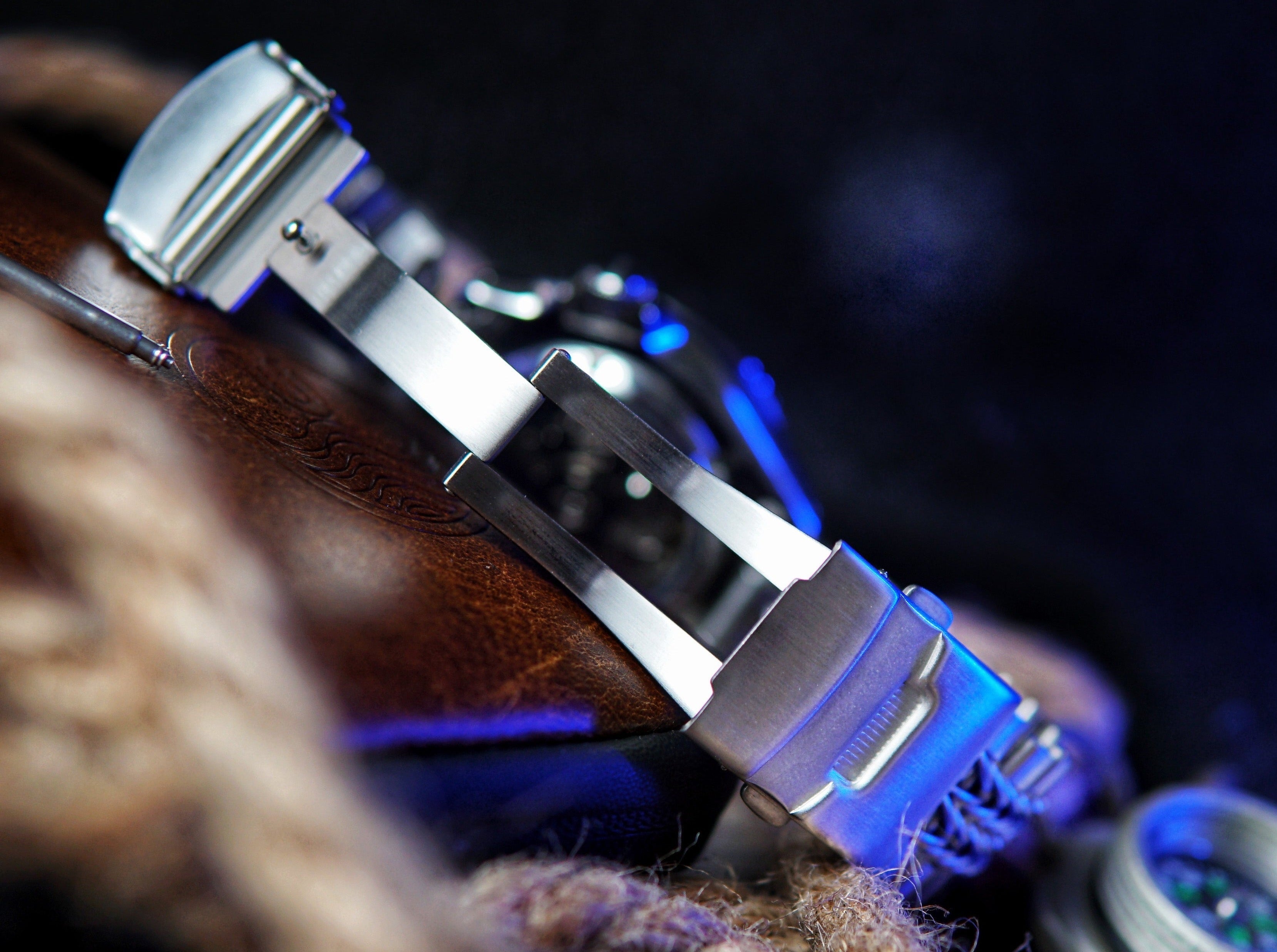 Blue and silver tactical bracelet with metal endlinks and paracord strap, displayed on wooden surface with military-style fastening