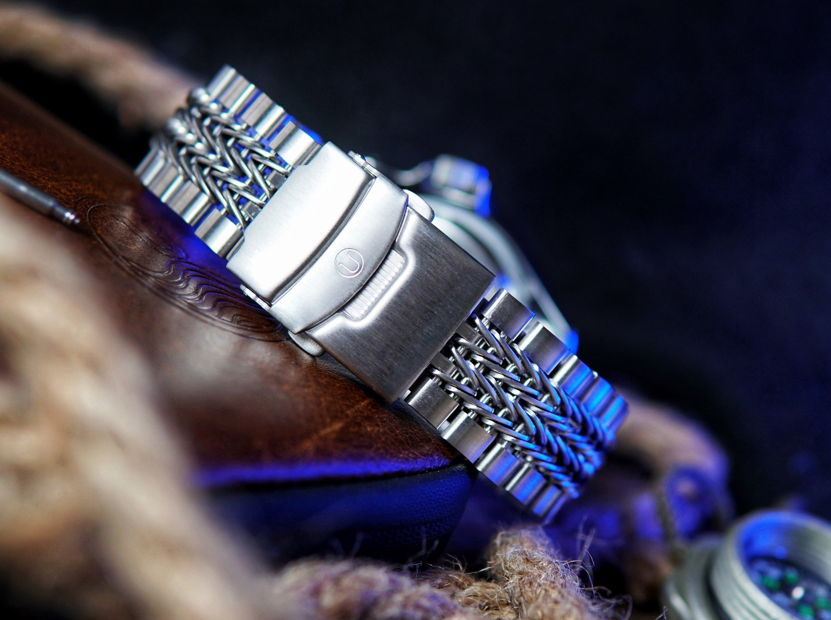 Stainless steel watch bracelet with razor-wire pattern links, polished center link, and fold-over clasp on dark textured background