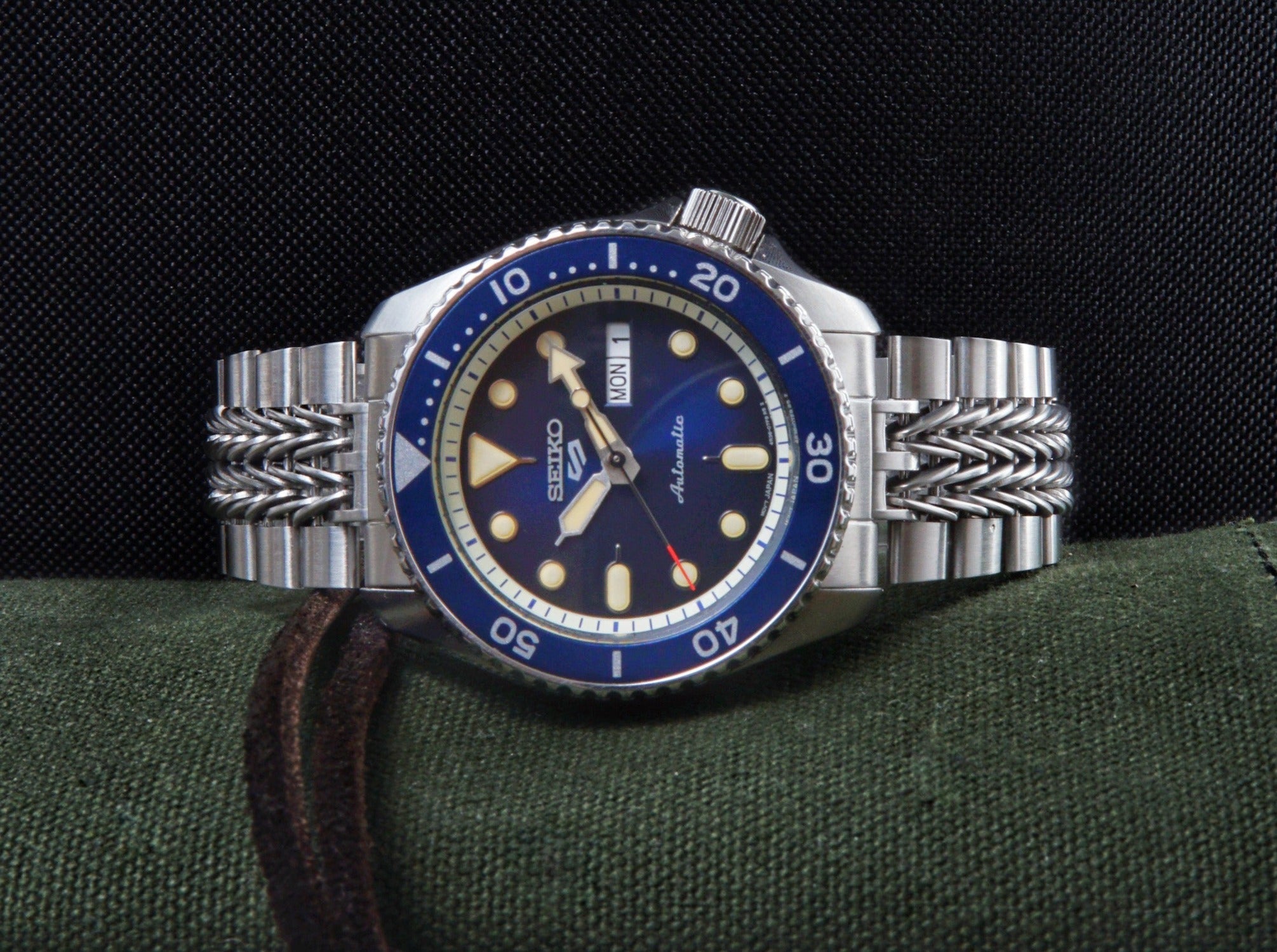 Seiko Prospex automatic dive watch with blue bezel, stainless steel bracelet, and day-date window on fabric background