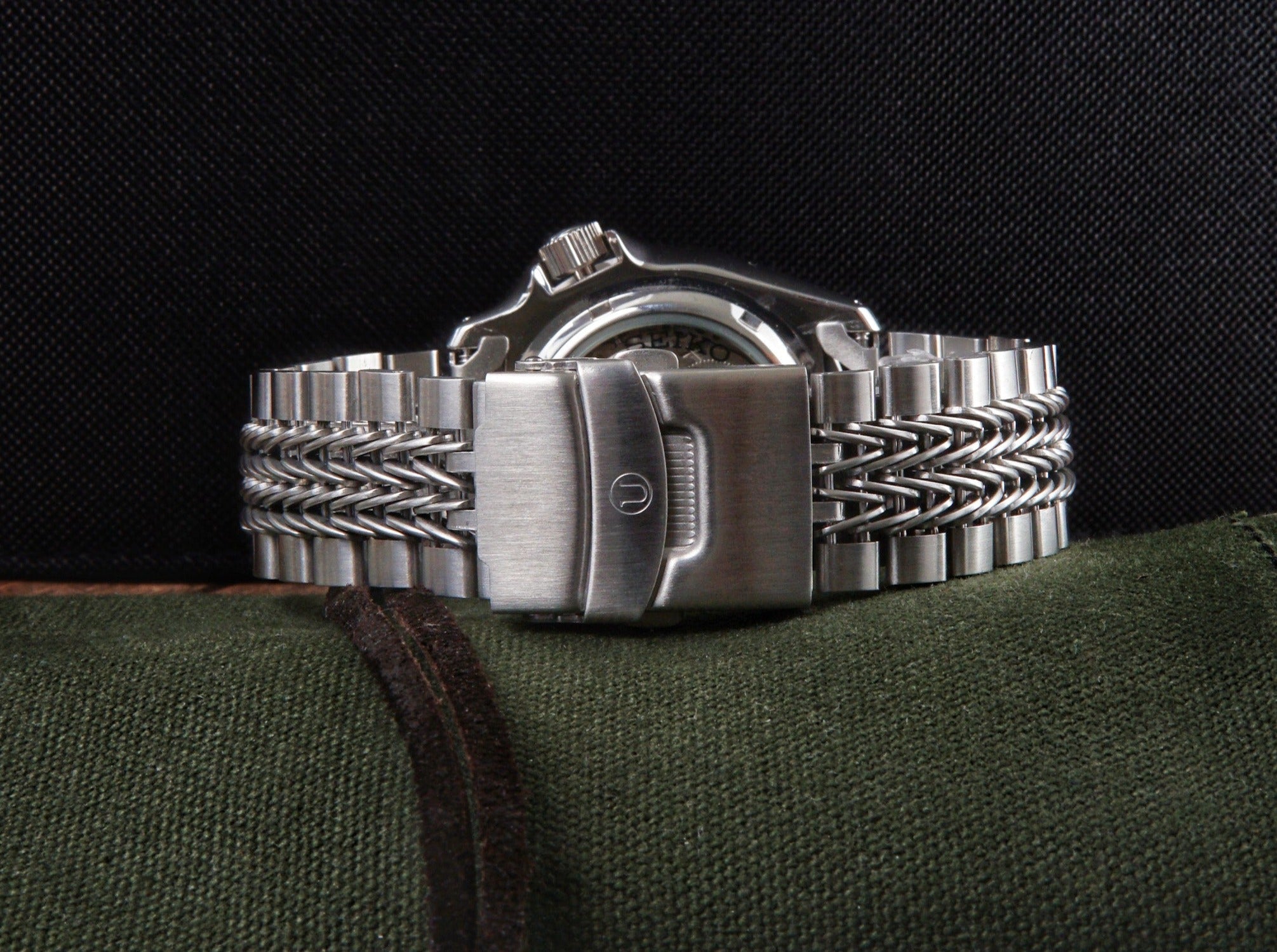 Stainless steel dive watch with linked metal bracelet and push-button clasp displayed on green fabric background