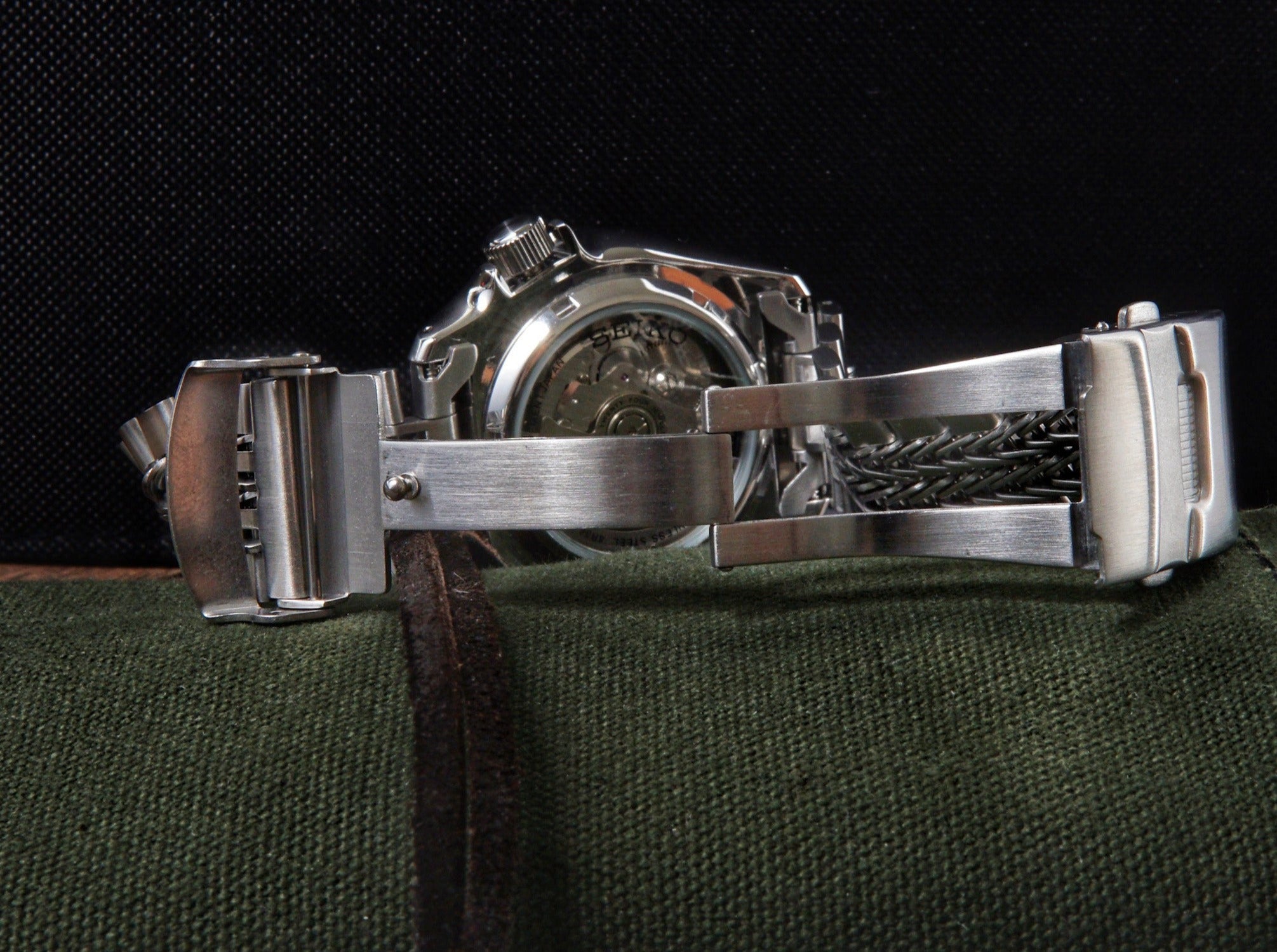 Stainless steel dive watch with razorwire bracelet on green fabric background, showcasing polished case and textured metal band detail