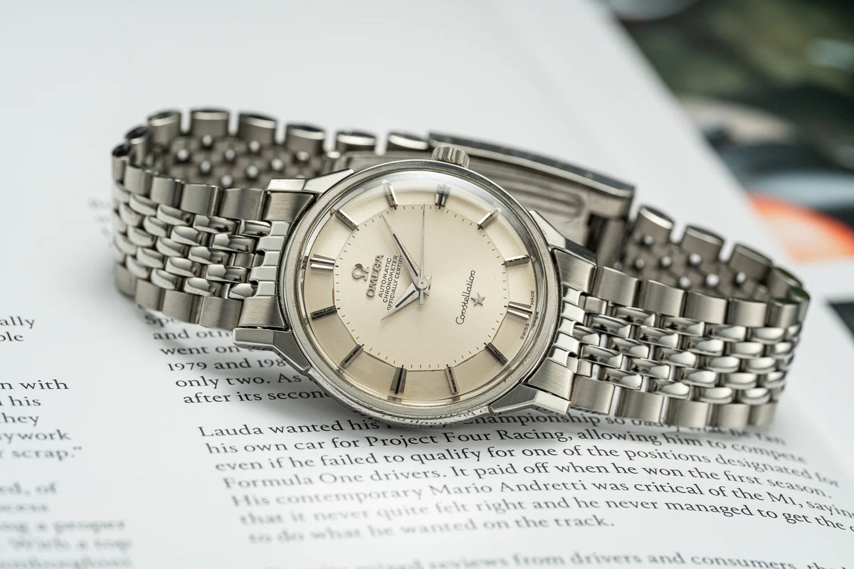 Omega Constellation vintage stainless steel watch with cream dial and integrated bracelet on magazine background
