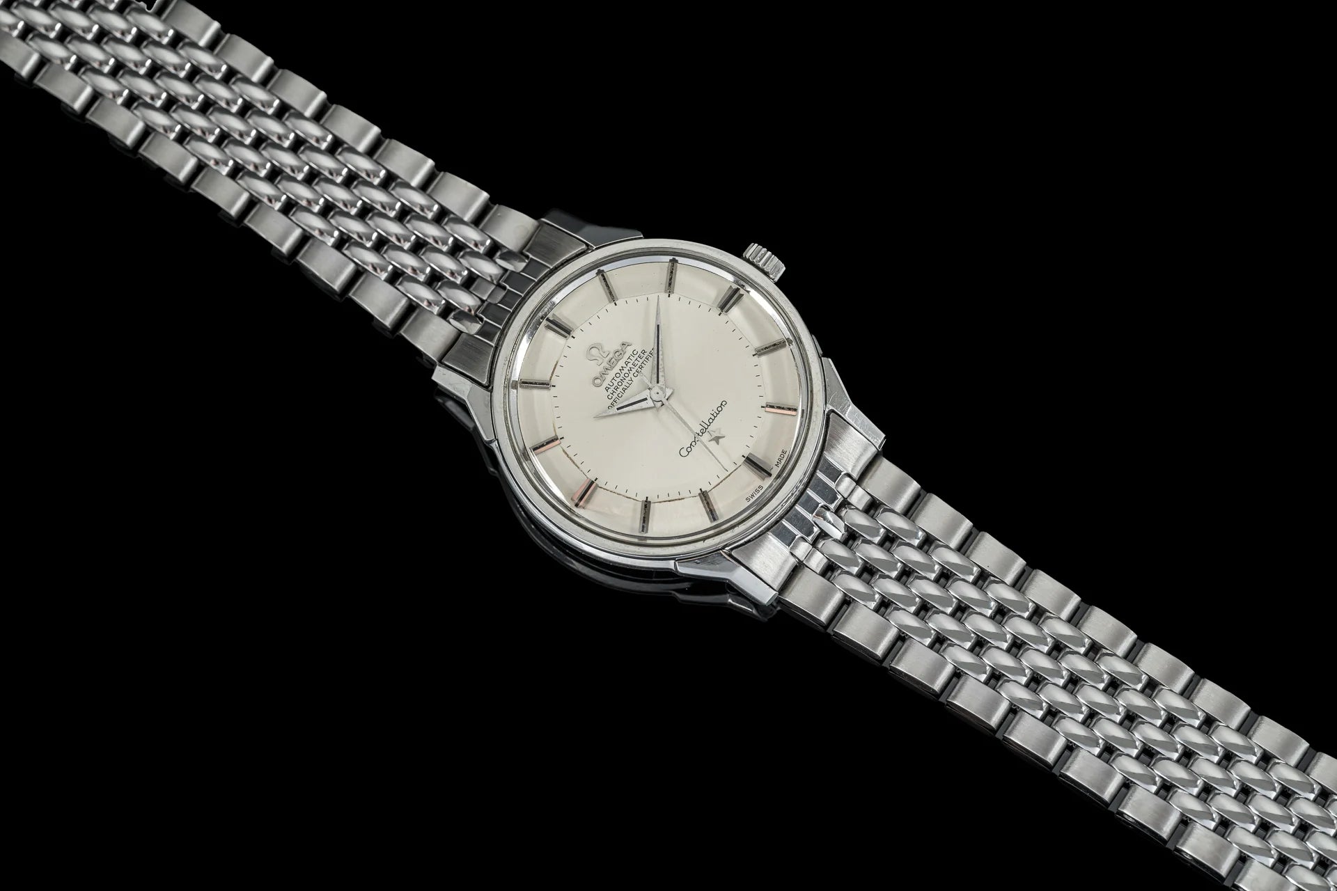 Silver Omega Constellation watch with cream dial, stainless steel beads of rice bracelet, and minimalist hour markers on black background