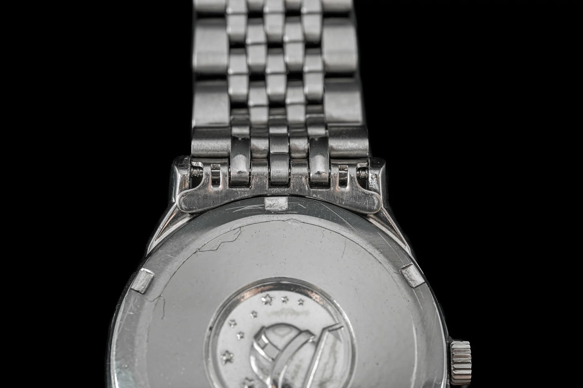 Stainless steel Omega Constellation watch with beads of rice bracelet and caseback detail on black background
