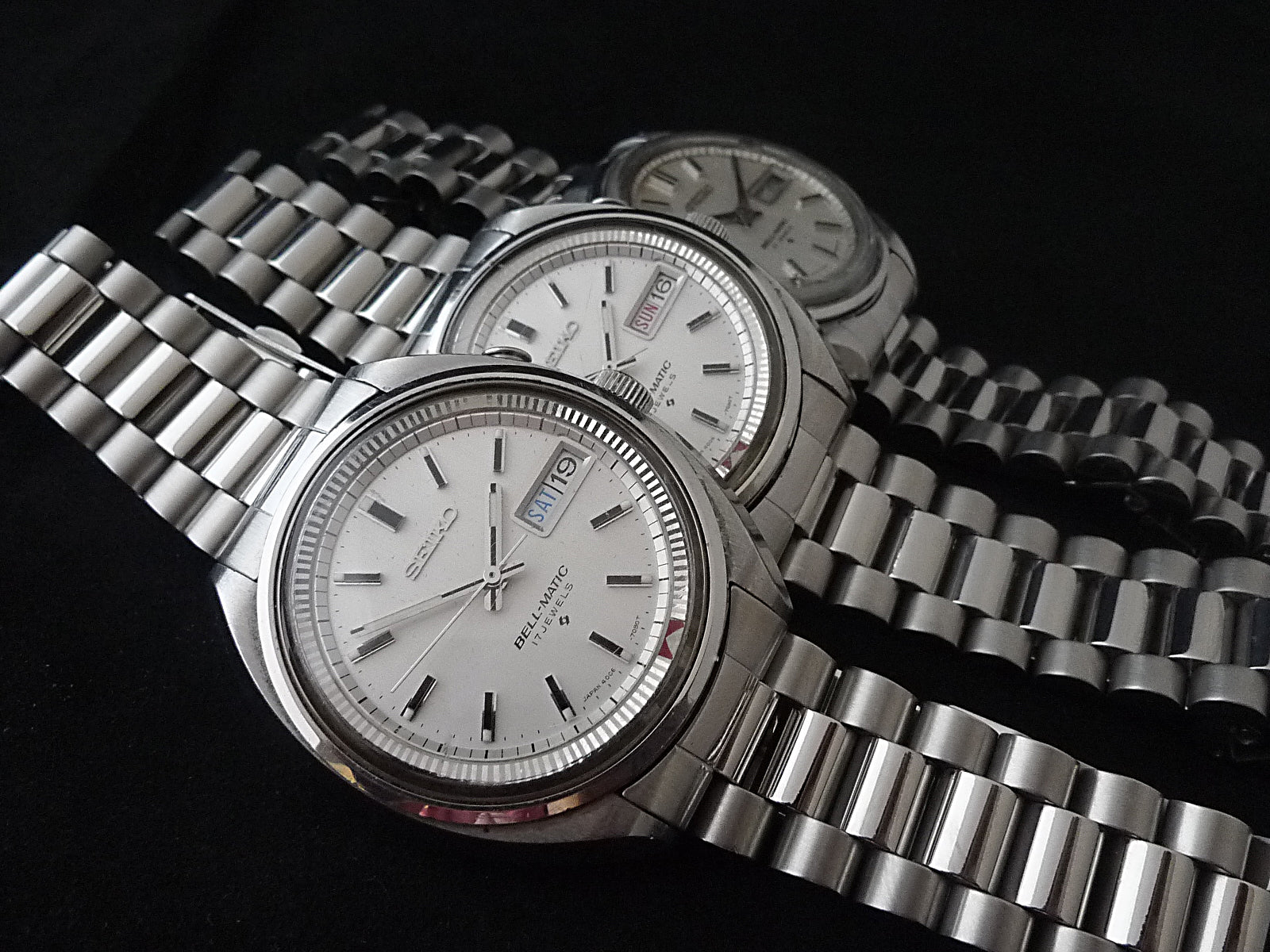 Three stainless steel Seiko Bell-Matic automatic watches with silver dials, day-date windows, and matching metal bracelets displayed on black background