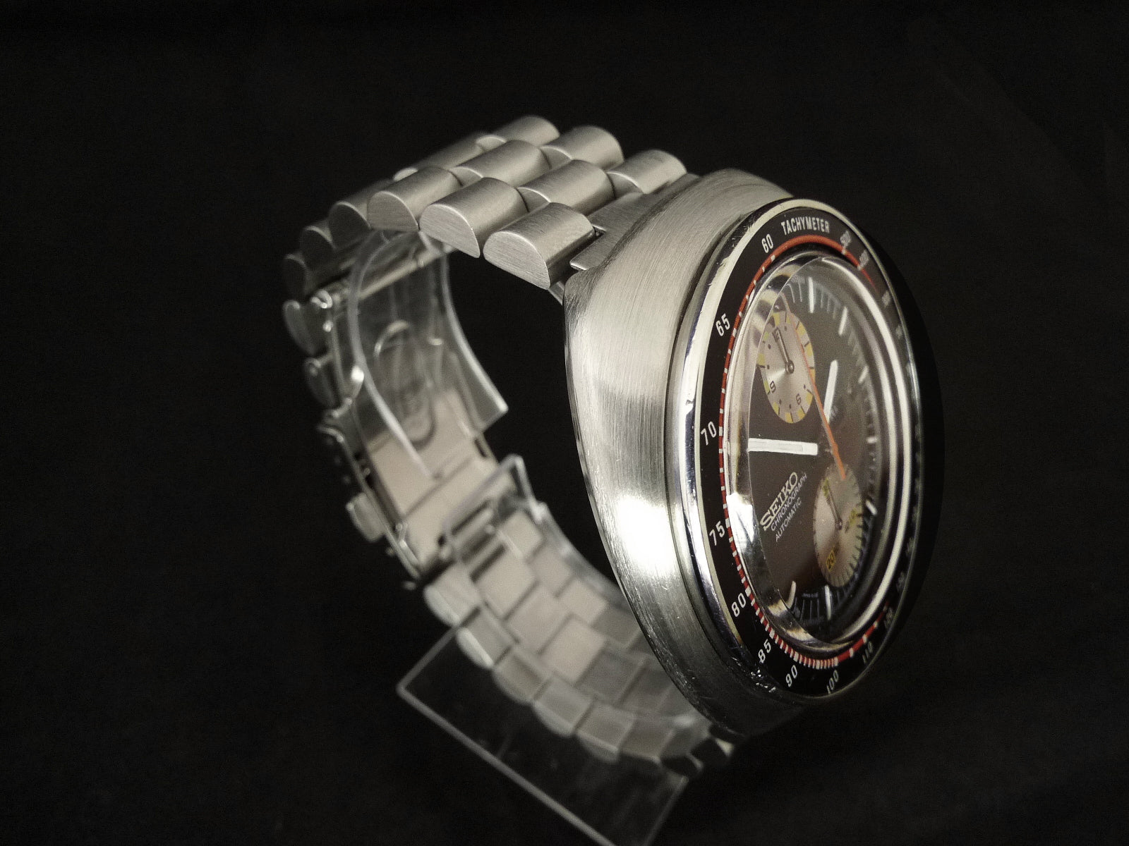 Stainless steel chronograph watch with tachymeter bezel, black dial, and matching metal bracelet on black background