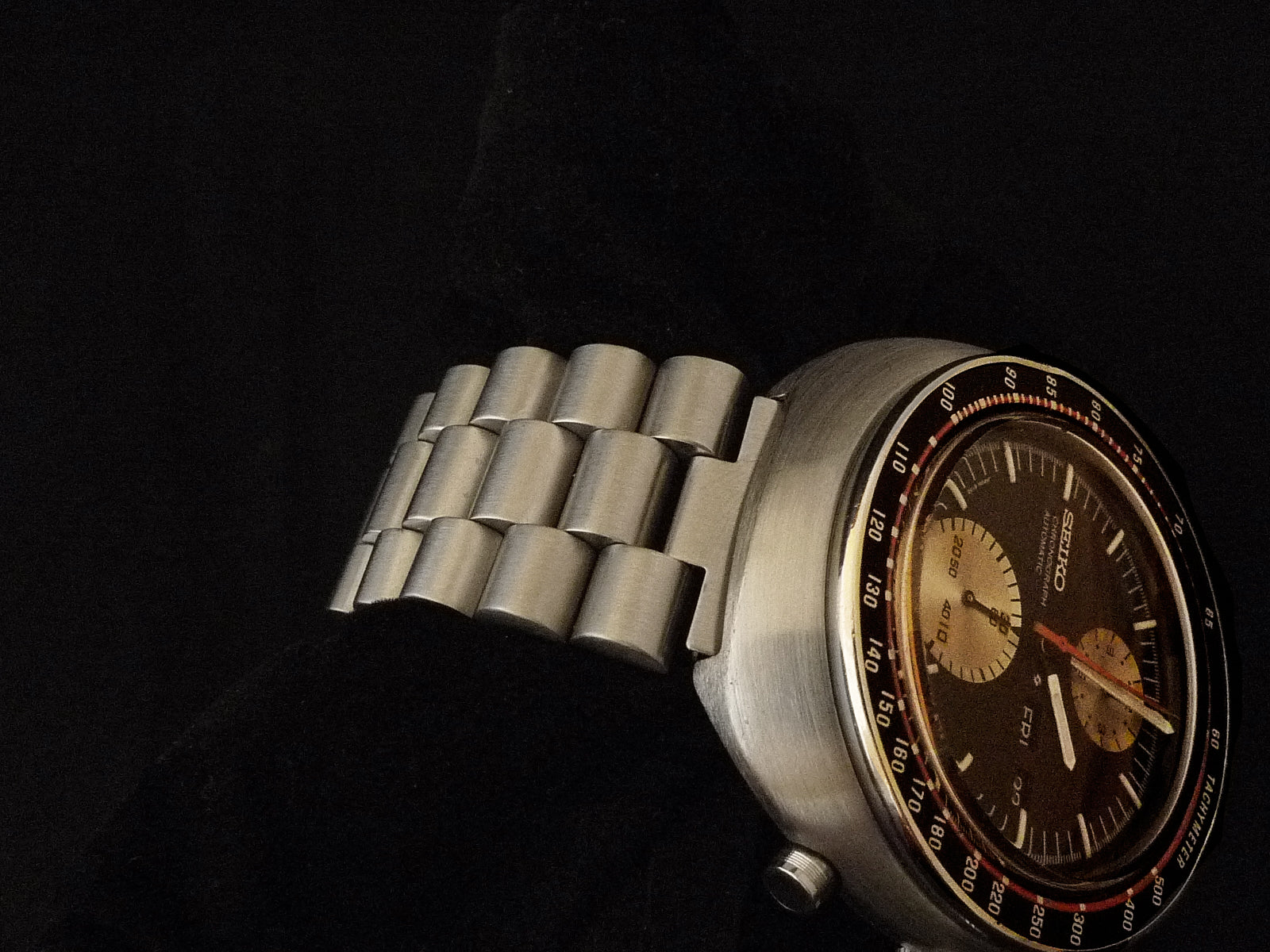Vintage Seiko 6138 chronograph watch with stainless steel bracelet and brown dial against black background