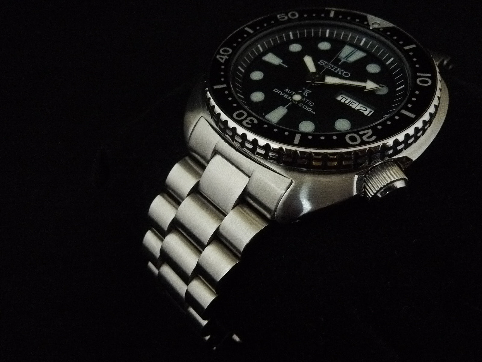 Seiko automatic dive watch with stainless steel bracelet, black dial, luminous markers, rotating bezel, and water resistance rating on dark background